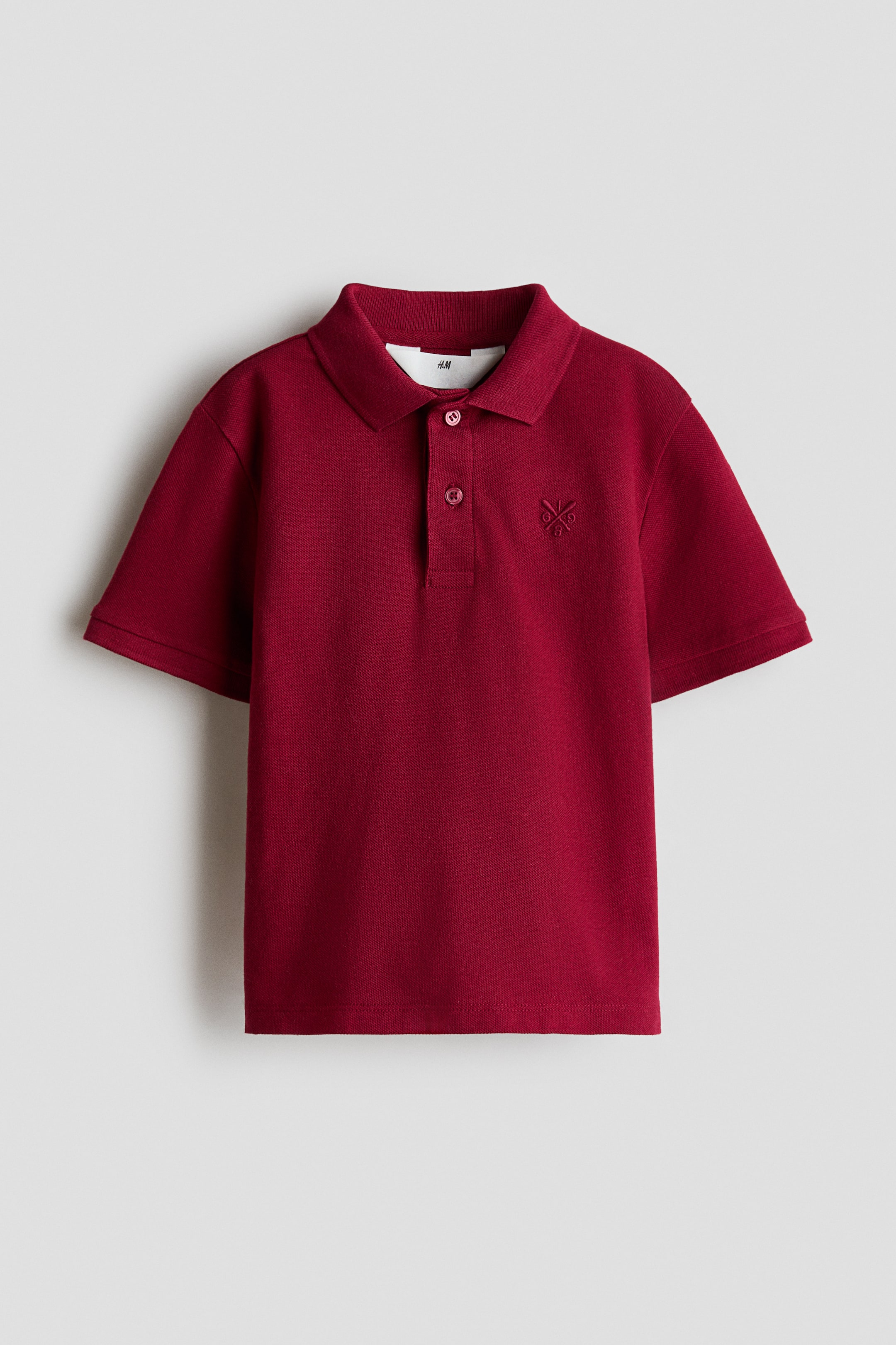 View larger image: The red polo shirt showcases a traditional fold-down collar, complemented by a two-button placket adorned with matching red buttons. It features short sleeves and an embroidered logo on the left chest. Inside the collar, a white brand tag is prominently visible.