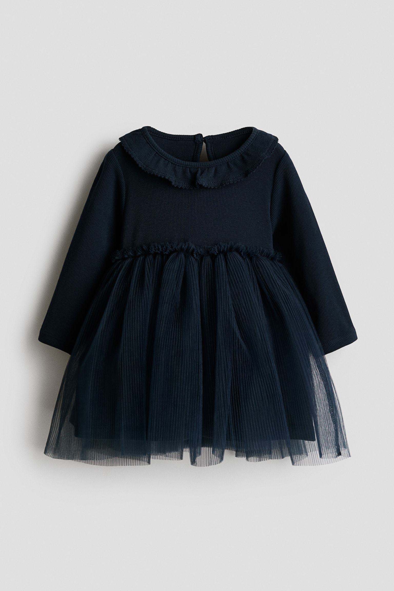 A navy blue long-sleeve dress is shown from the front, featuring a ribbed bodice with a frill-trimmed round neckline and a matching frilled waist. The dress is finished with a flared, layered tulle skirt.