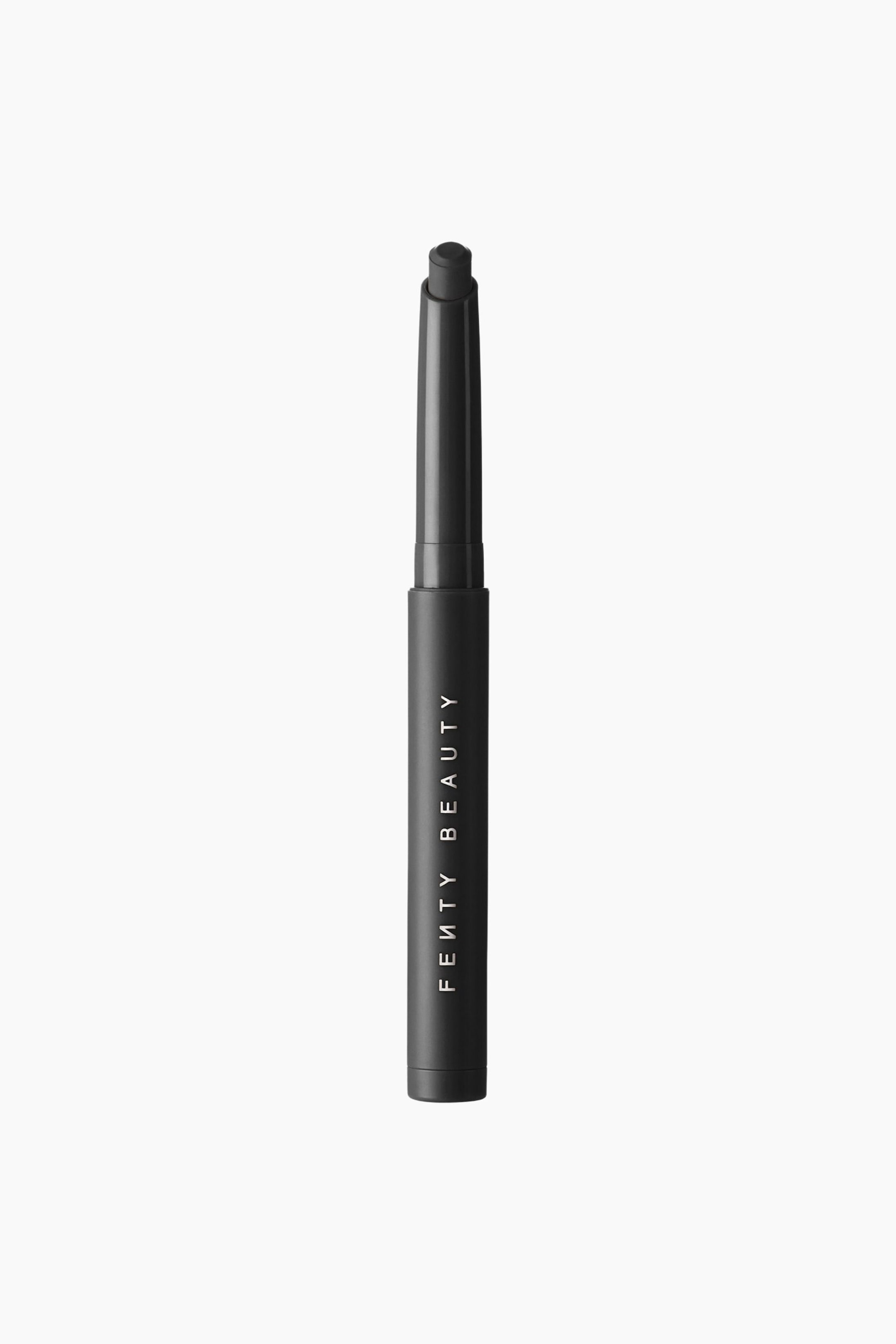 Se større billede: Shadowstix Longwear Eyeshadow Stick står lodret og fremhæver sin matte sorte cylindriske hylster med "FENTY BEAUTY" trykt lodret i hvide bogstaver. Den åbne top afslører en afrundet, mørkegrå øjenskyggetip, der stikker frem fra en let blank inderhylster.