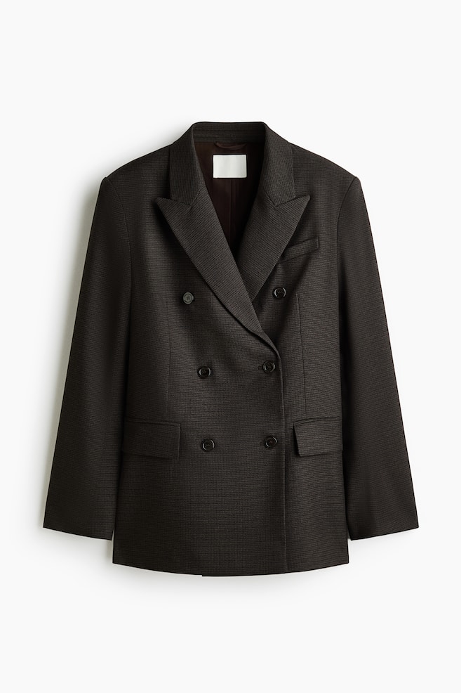 En mÃ¸rkebrun, teksturert dobbeltkneppet blazer vises forfra, og fremhever brede slag med spiss fasong, strukturerte skuldre og en frontlukking med seks knapper. Designet inkluderer en brystlomme med passpoil, to frontlommer med klaff og en skreddersydd, lang silhuett. - 1