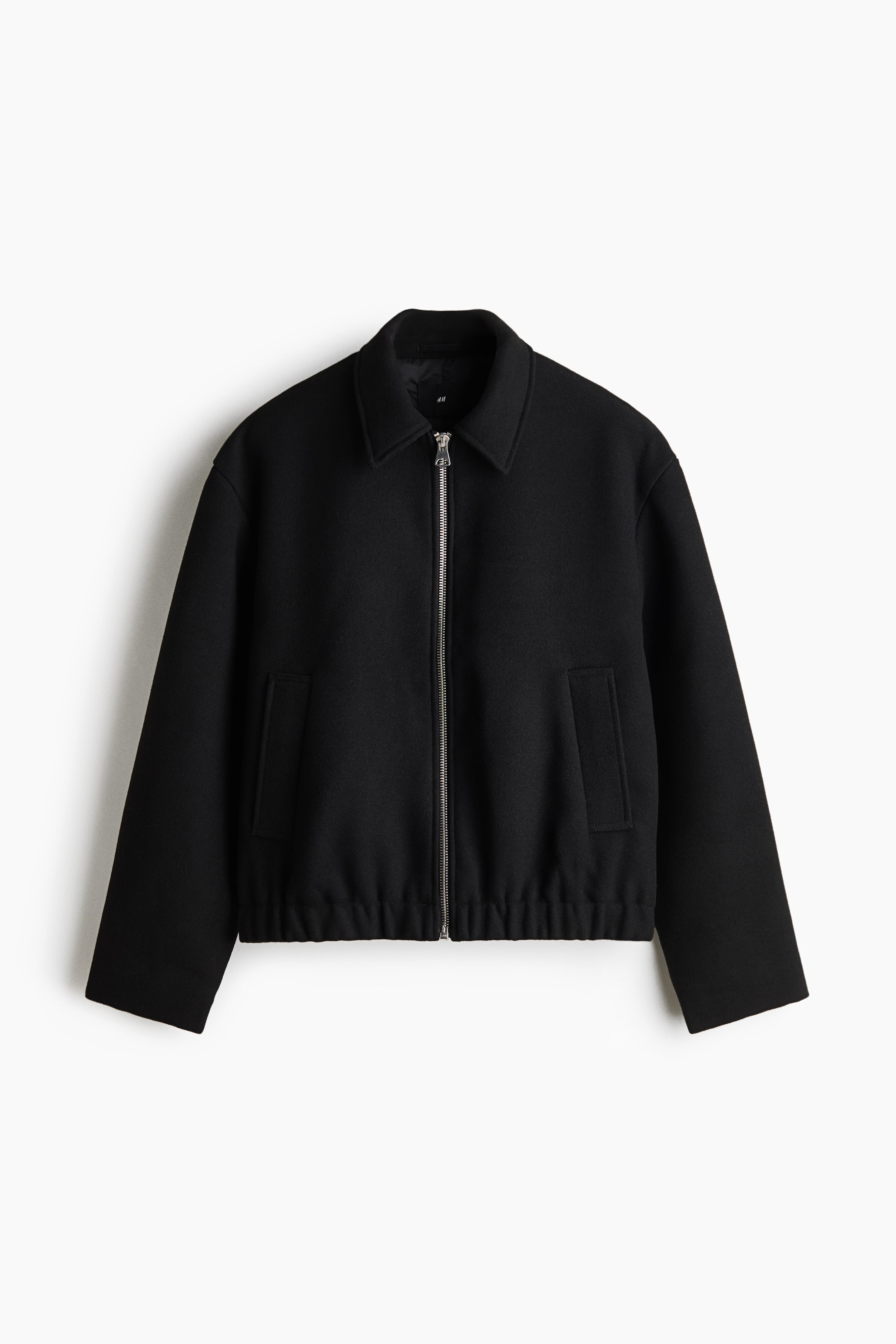 View larger image: A black zip-up jacket is shown from the front, featuring a pointed collar, a silver-toned metal zipper, and two vertical welt pockets. The jacket has dropped shoulders, long straight sleeves, and a gathered elastic hem.