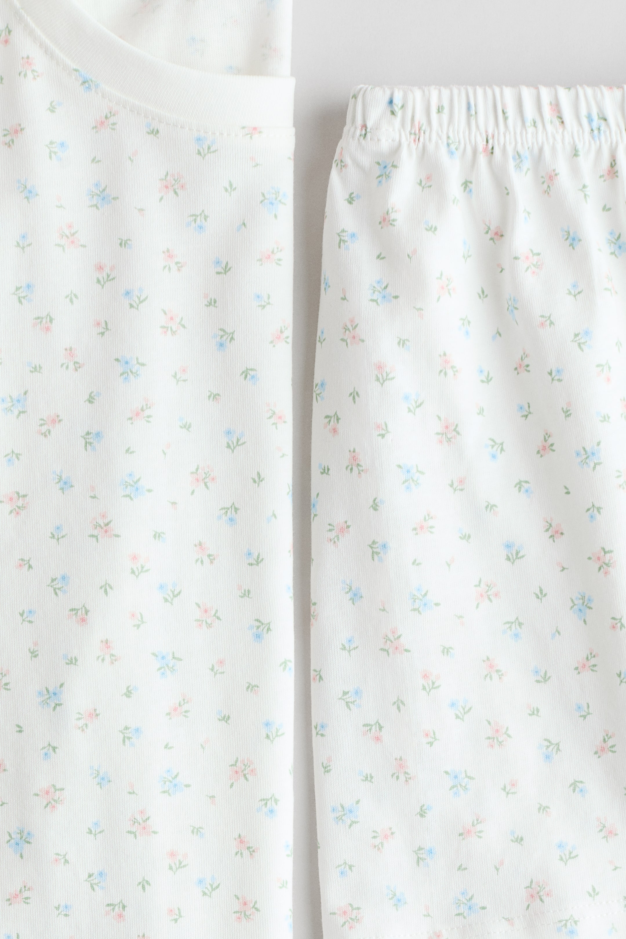Größeres Bild ansehen: Ein Pyjama-Set, in FRONT-Ansicht dargestellt, zeigt einen weißen Baumwoll-Jersey mit kleinem Blumenmuster in hellblau und rosa. Das Oberteil verfügt über einen Rundhalsausschnitt, die Shorts haben einen elastischen Bund.