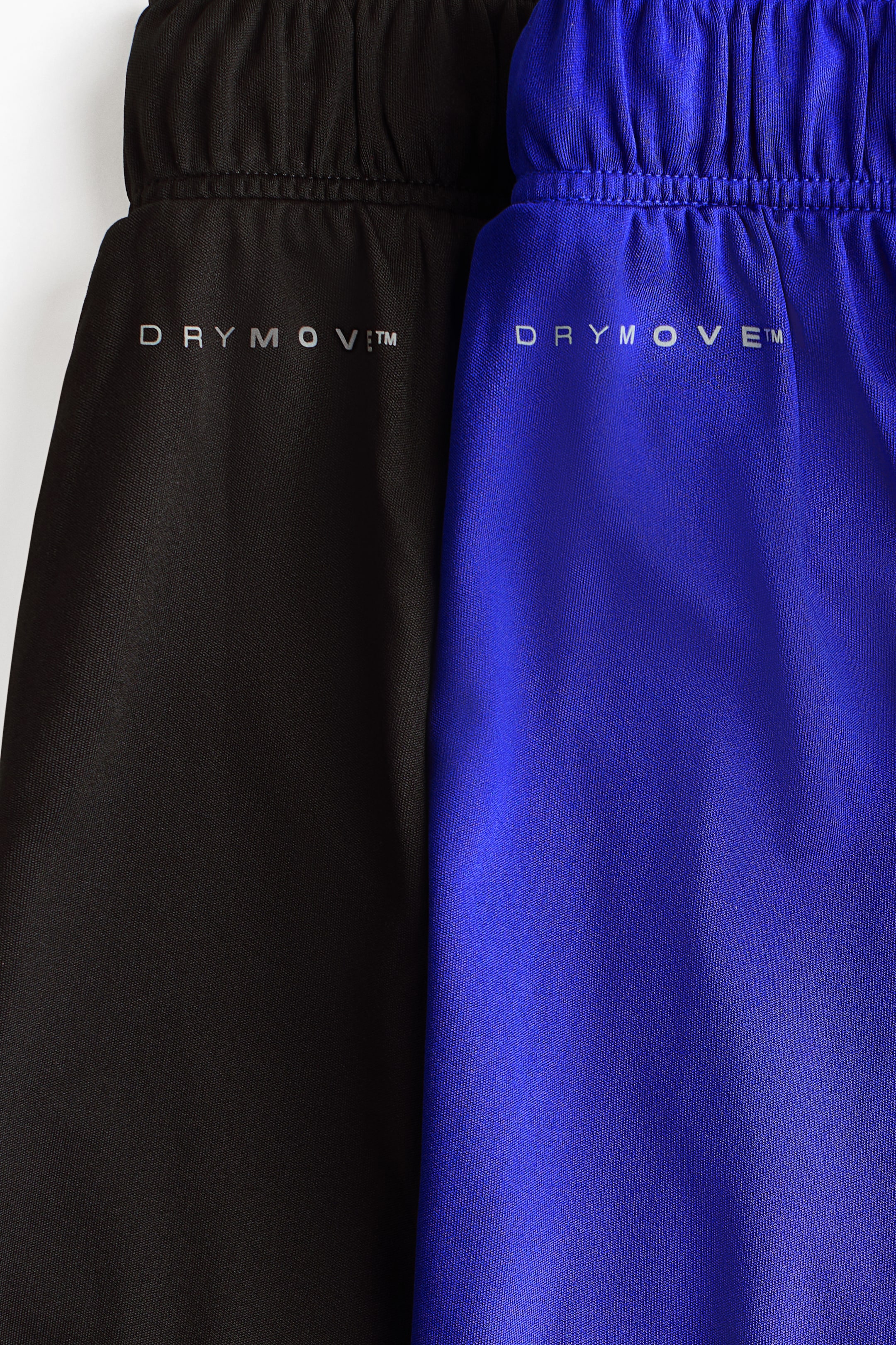 Größeres Bild anzeigen: Ein 2er-Pack Fußballshorts zeigt seine oberen Vorderteile, wobei eine Shorts in Schwarz und die andere in Blau ist. Beide Shorts verfügen über geraffte, elastische Taillenbänder und das "DRYMOVE?"-Logo, das in Silber unterhalb der Taille aufgedruckt ist.