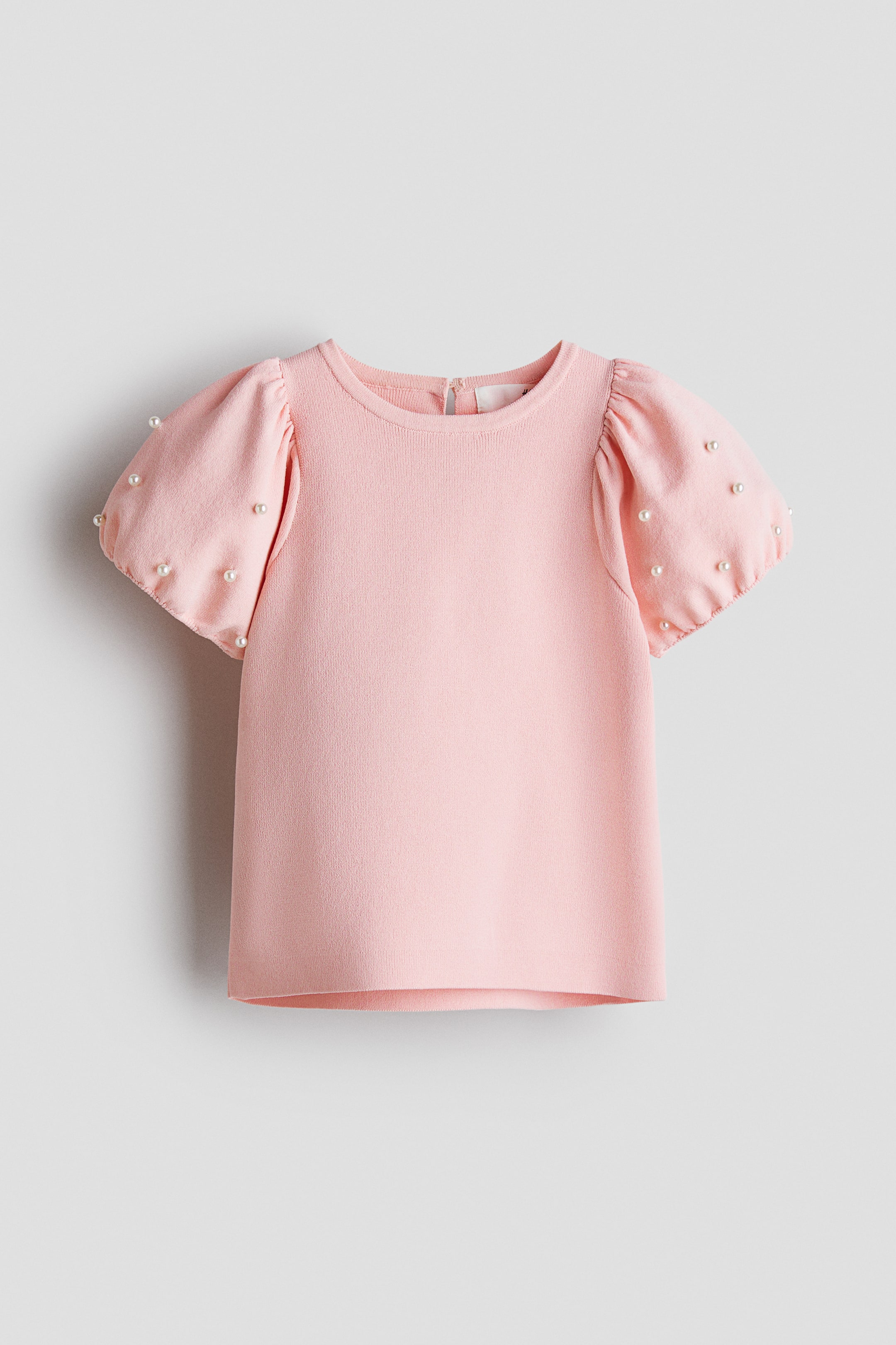 הצגת תמונה גדולה יותר: חולצת סריג ורודה מציגה מבט קדמי, עם מחשוף עגול ושרוולים קצרים ונפוחים. חרוזי פנינה קטנים מעטרים את שני השרוולים, ורוכסן קצר נראה בגב הצוואר.