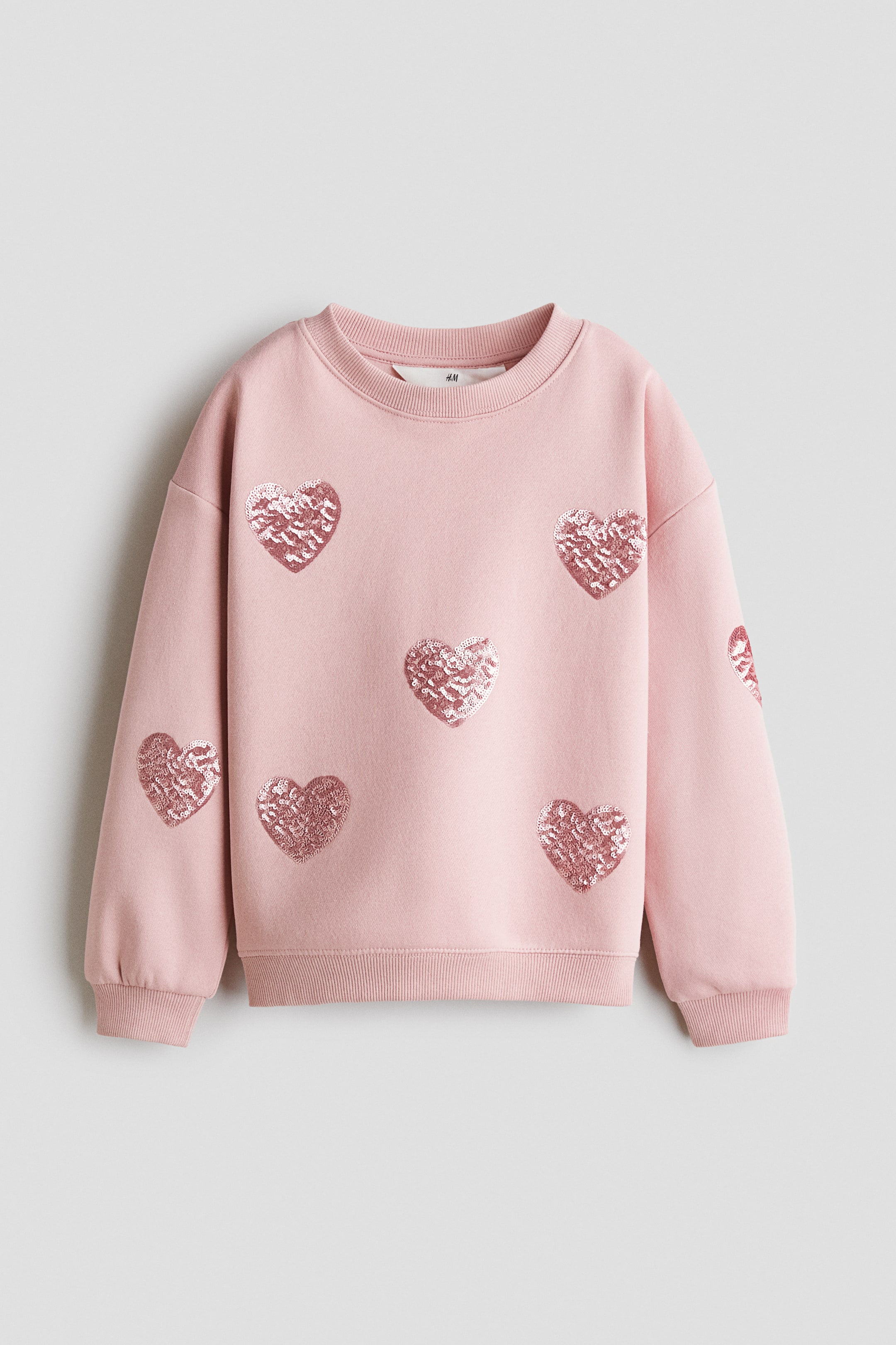 View larger image: A pink sweatshirt is laid flat, featuring a ribbed crew neck, ribbed cuffs, a ribbed hem, and multiple pink sequin hearts scattered across the front and sleeves.