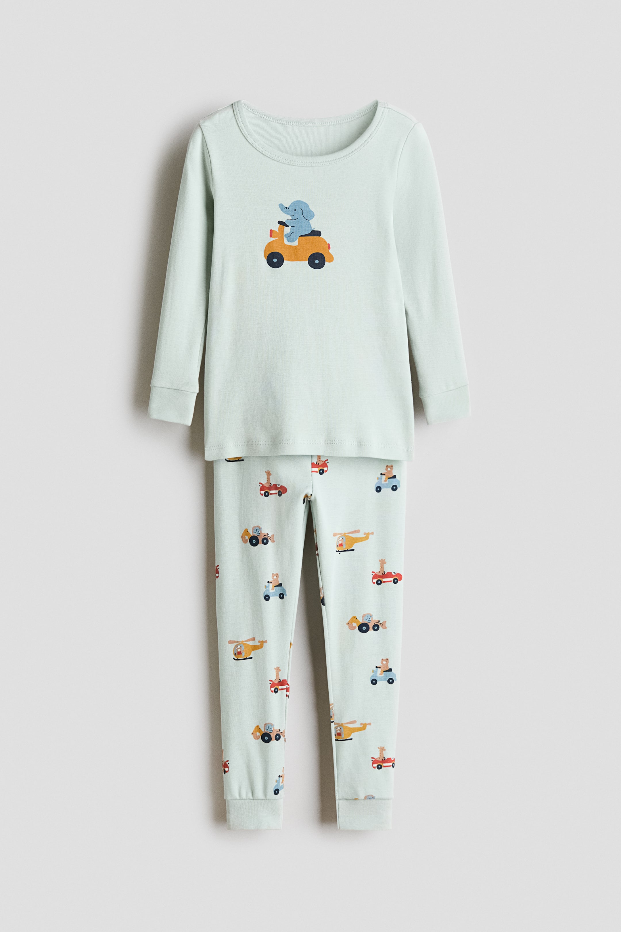 View larger image: Snug Fit printed cotton pajamas are presenting FRONT, featuring a light green long-sleeved top with a round neck and an elephant riding a scooter printed on the front. The matching long trousers are displaying an allover print of various animals riding vehicles, and both pieces are finished with ribbed cuffs.
