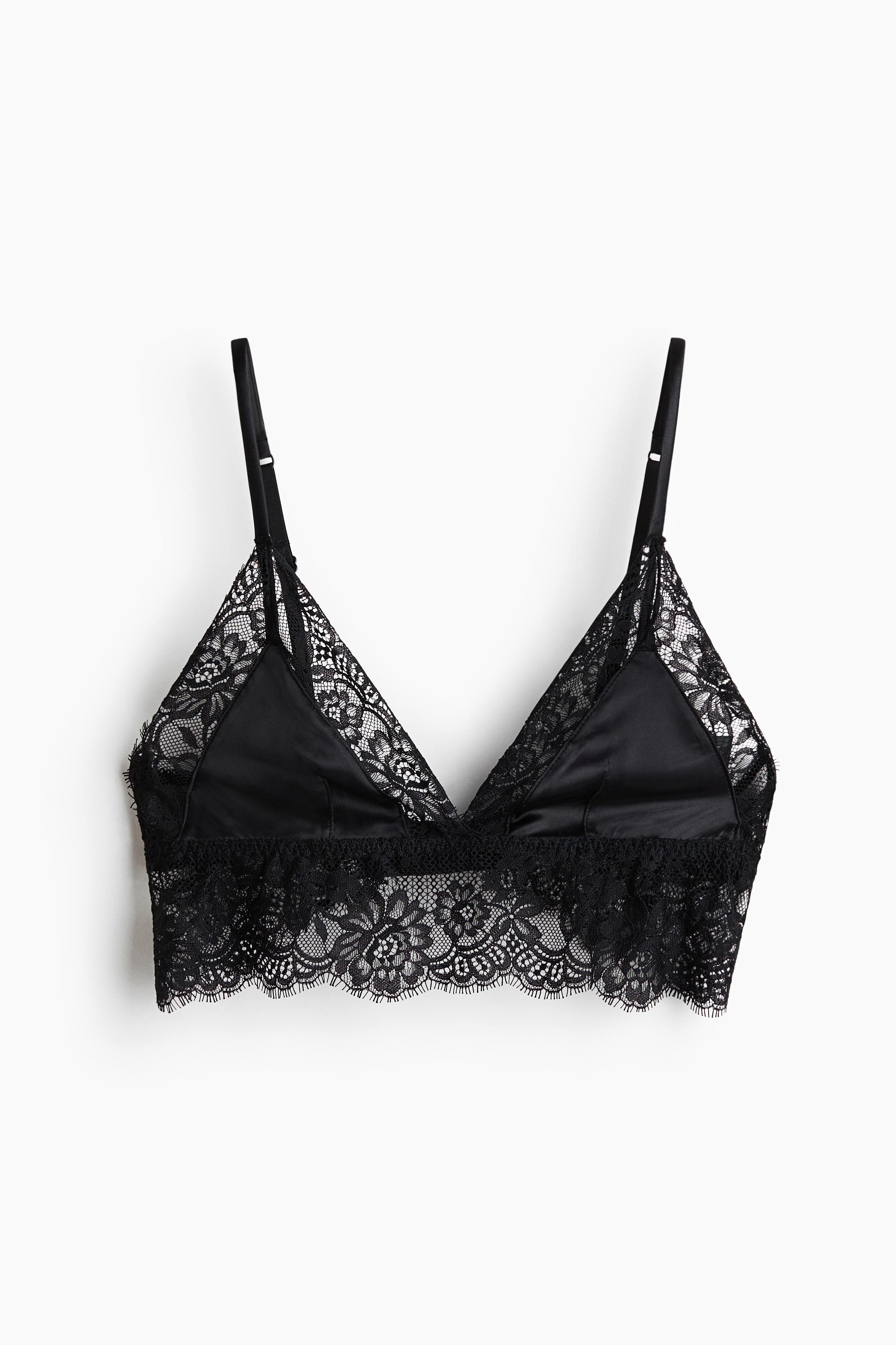 A black soft cup bra in satin and lace is being worn by the model, featuring triangular satin cups with eyelash lace trim and a wide lace underband. The bra is styled with matching black satin and lace briefs that are partially visible.