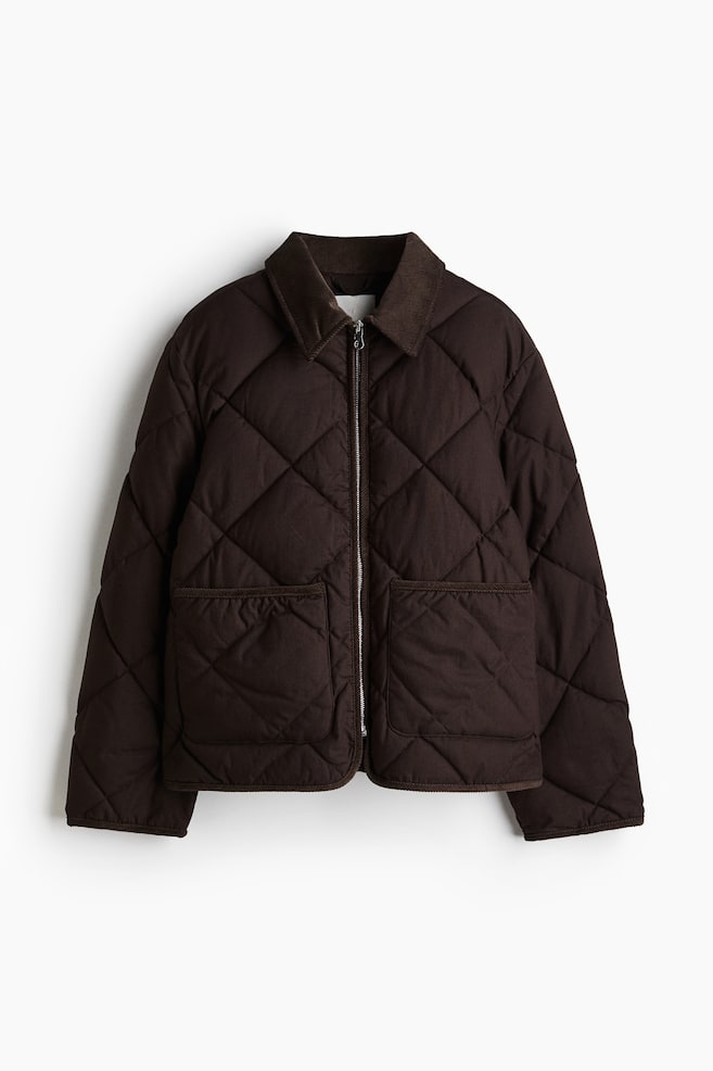 A dark brown, lightly padded jacket is shown from the front. It is made of quilted cotton canvas and features a corduroy collar, a silver zip down the front, two patch pockets on the lower front, gently dropped shoulders, and long sleeves. - 1