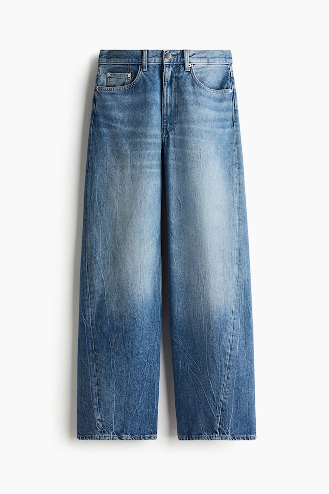 A pair of medium blue, wide-leg denim jeans is presented from the front, featuring a faded wash with lighter areas on the thighs and knees. It includes a five-pocket style, button and zipper closure, and visible creasing throughout the fabric. - 1