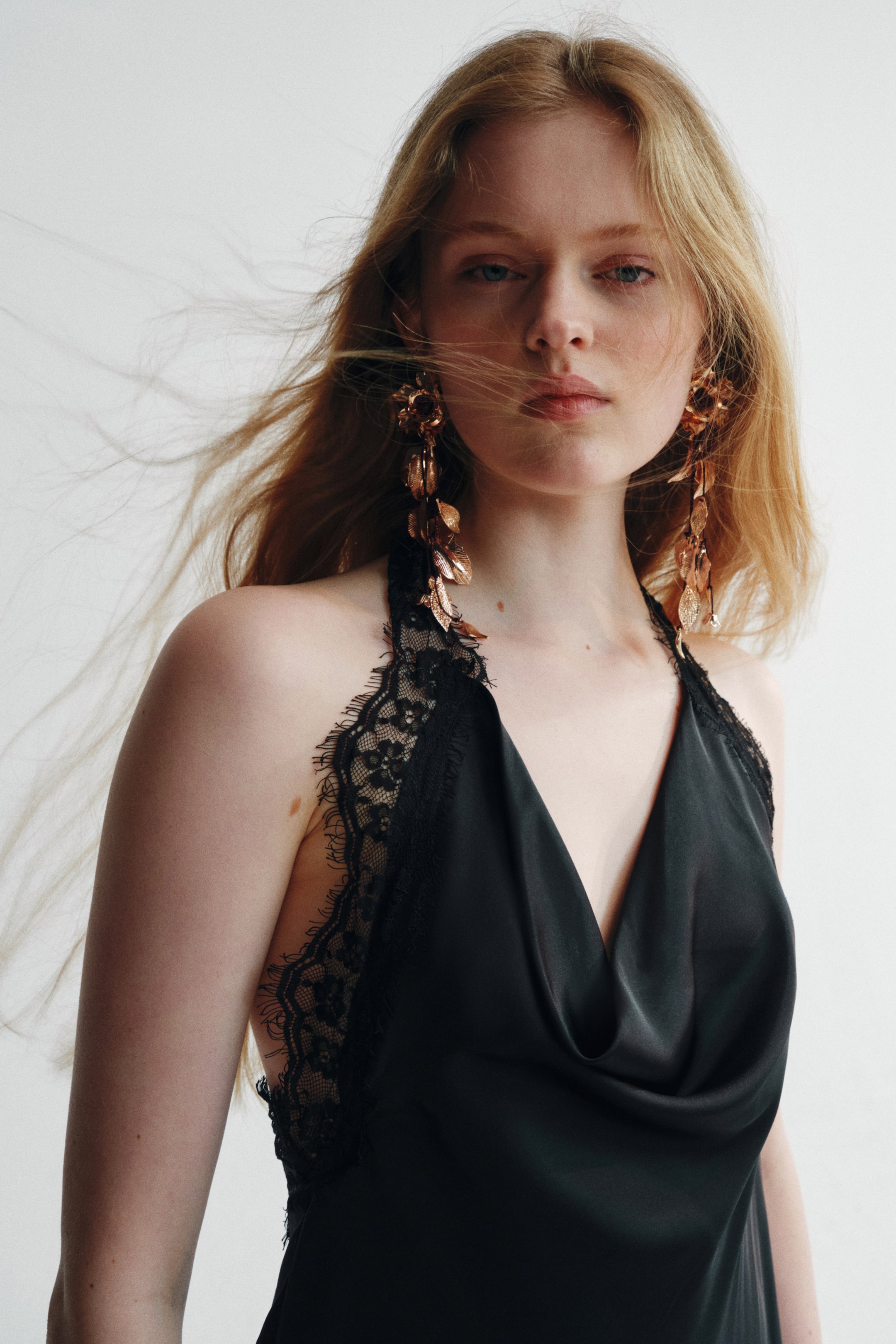 View larger image: The model is adorned with rose gold-toned metal earrings, showcasing a flower-shaped top piece and long, cascading strands embellished with metal leaves. These earrings perfectly complement the model's black top with lace trim.