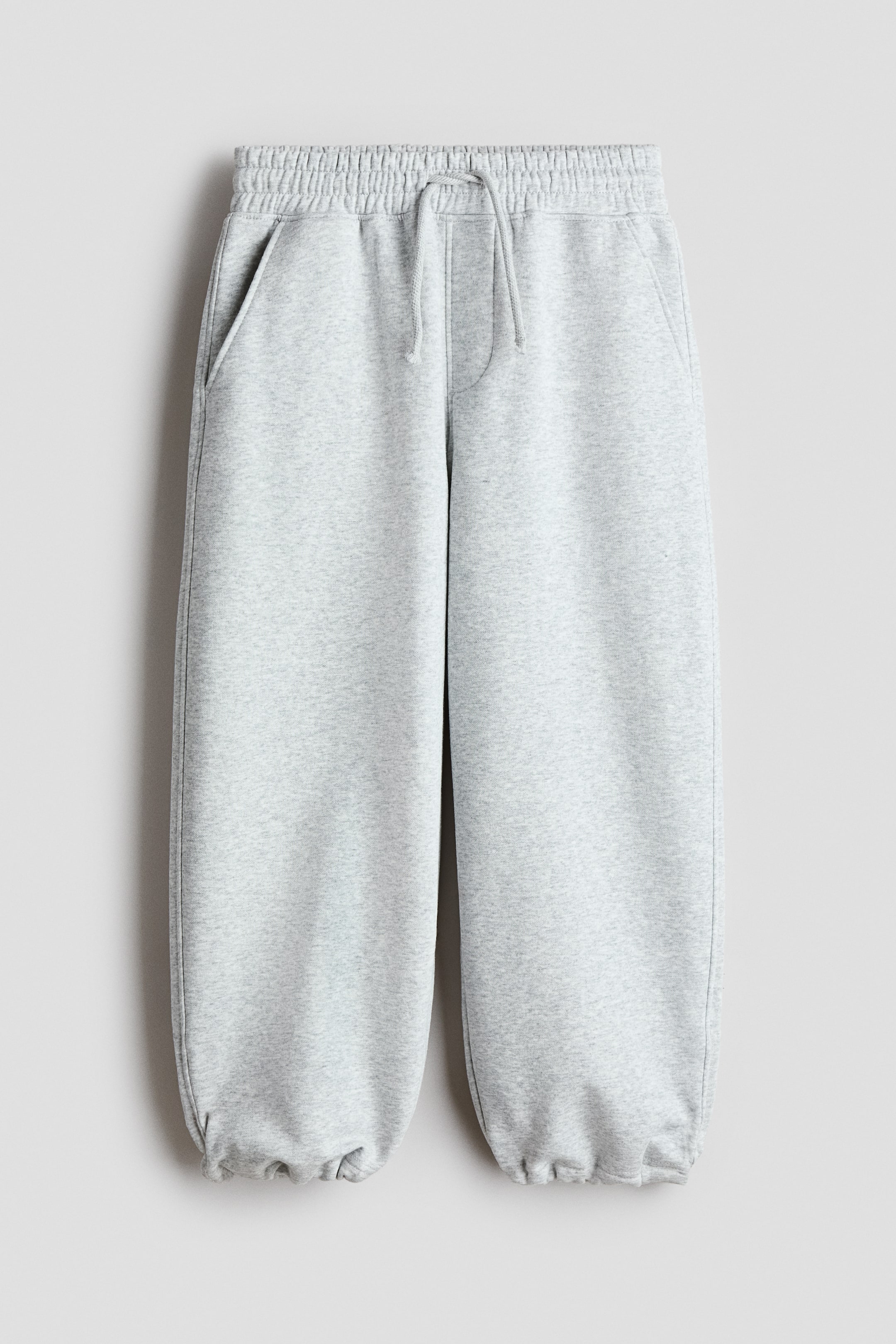 Visualizza immagine più grande: "Joggers in felpa color grigio chiaro melange con vita elasticizzata e coulisse, patta finta e tasche laterali diagonali. Le gambe a palloncino terminano con orli elasticizzati a coulisse."