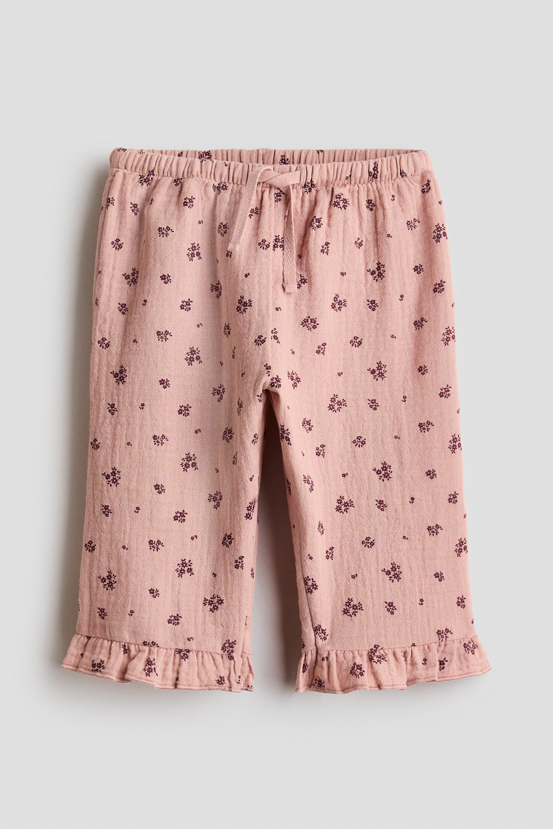 View larger image: These pink trousers showcase a dark floral design, complete with an elasticated drawstring waistband and ruffled hems at the cropped leg openings.