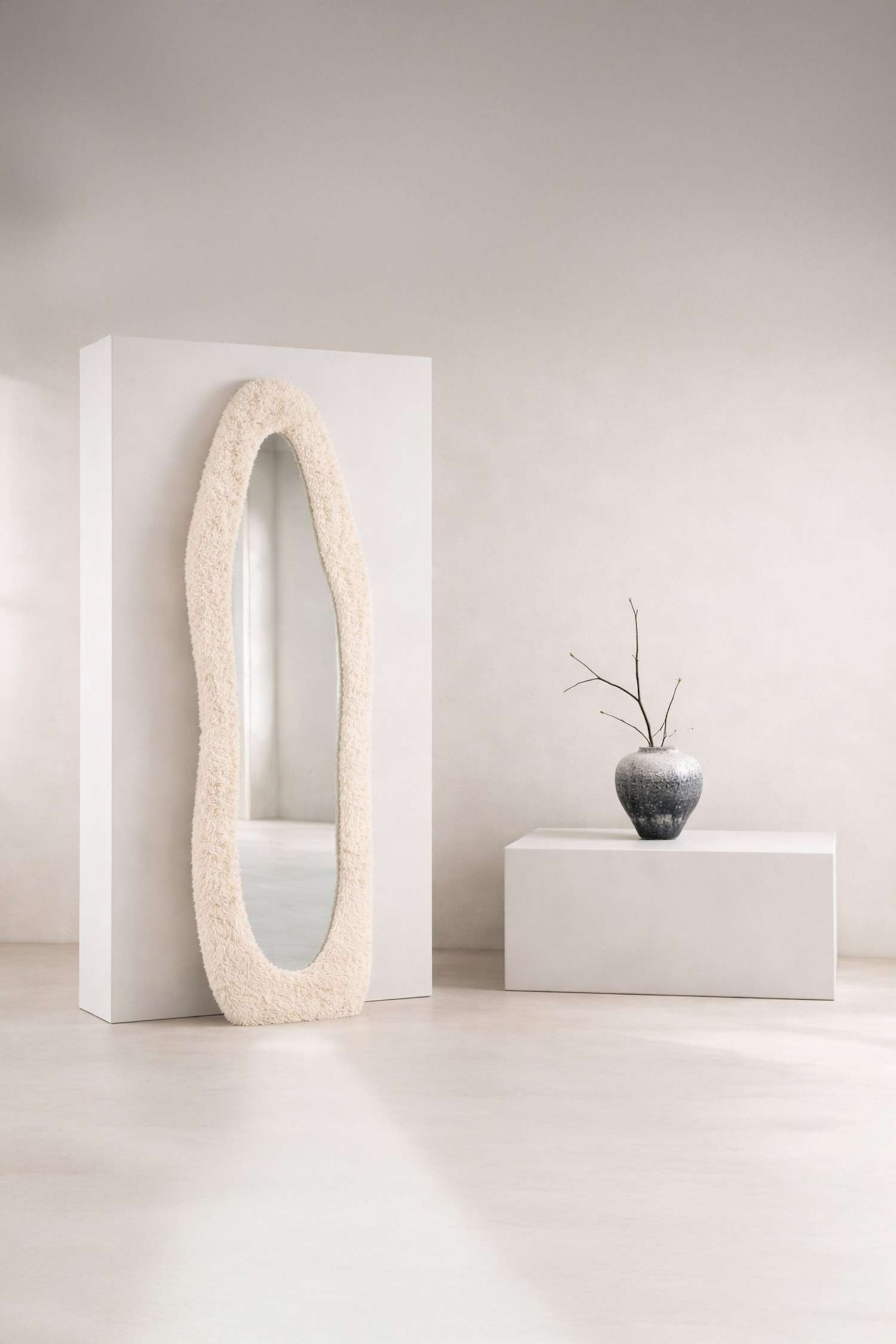 Agrandir l'image: Un miroir en pied se tient debout, arborant une forme irrégulière et ondulée. Son cadre est recouvert d'un tissu bouclé de couleur crème.