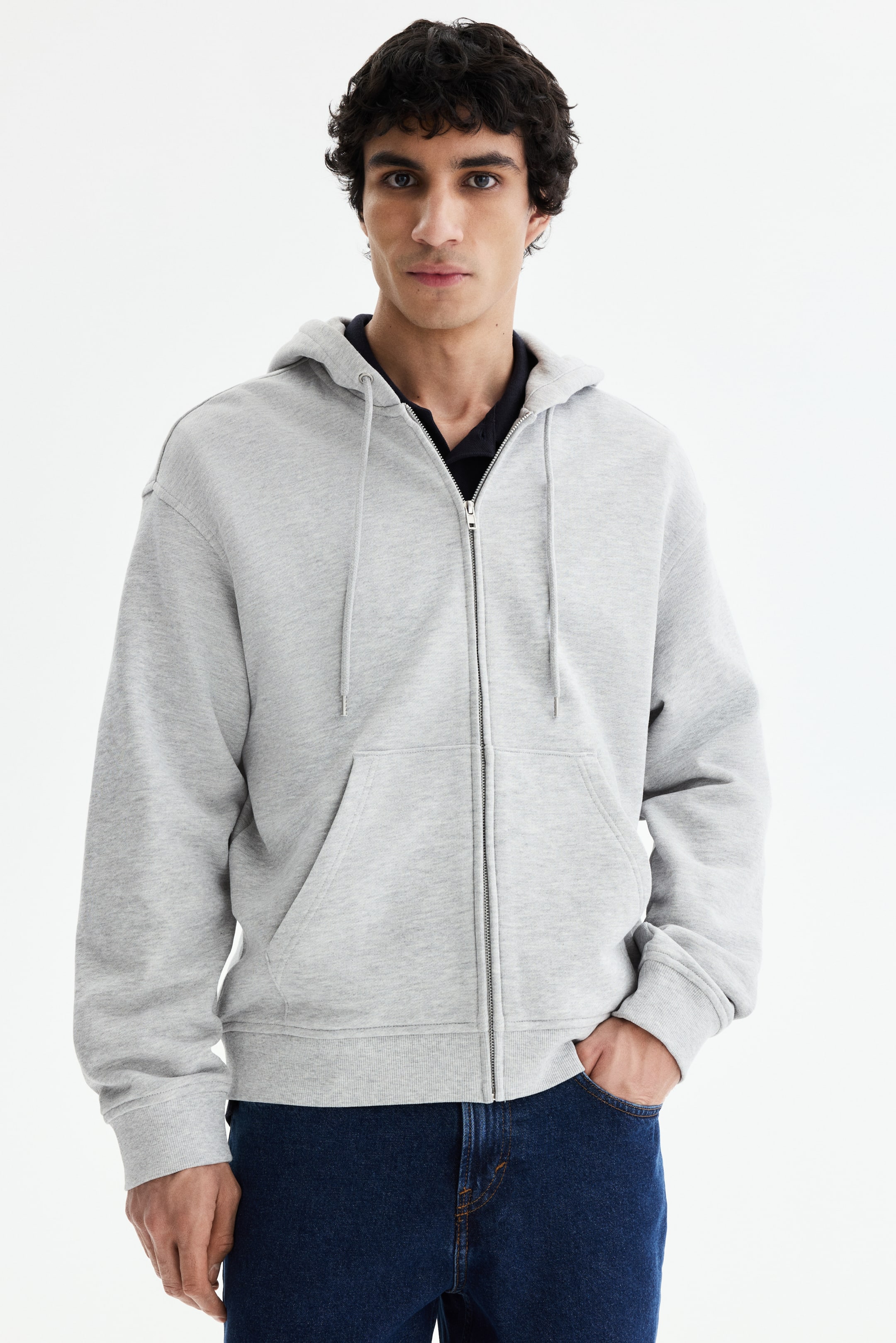 View larger image: A light grey zip-up hoodie is showcased facing forward, featuring a full-length zipper, a kangaroo pocket, and drawstrings on its hood. It displays ribbed cuffs and a ribbed hem, layered over a dark polo shirt.
