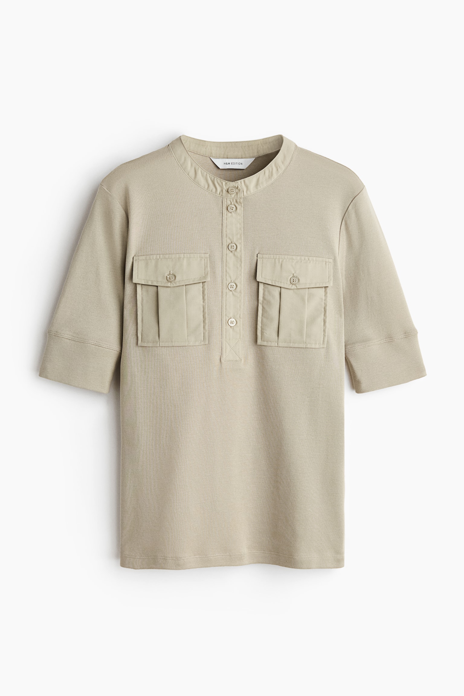 A light beige fitted, short-sleeved top is shown from the front, featuring a narrow-ribbed jersey body. It showcases a band collar and a four-button placket crafted from a contrasting woven fabric with a slight sheen, along with two bellows chest pockets, each with a flap and button fastening. - 1