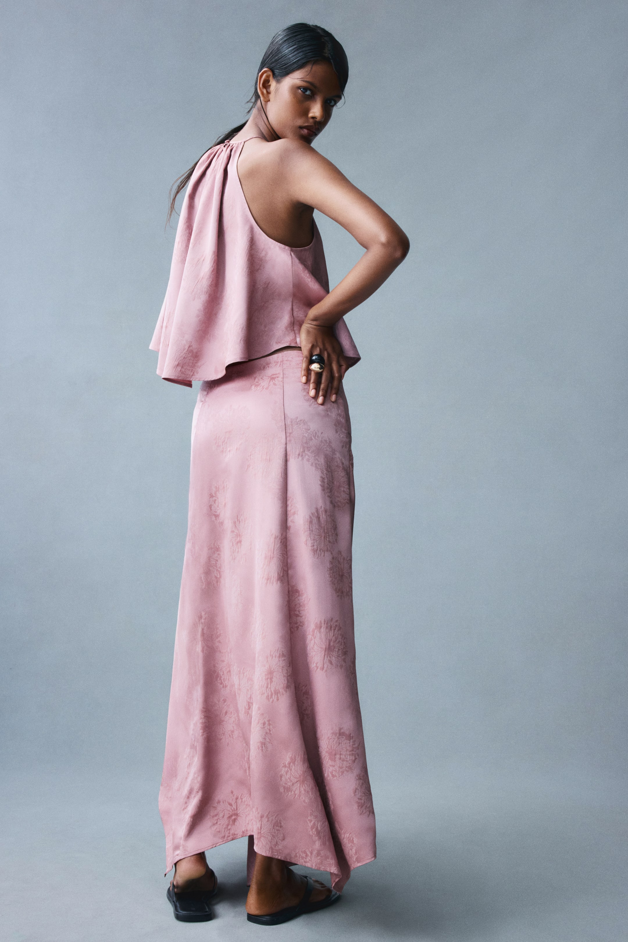 View larger image: A short, sleeveless top in a patterned dusty pink woven fabric is worn by the model with a matching maxi skirt. The top features a loose, draped fit with gathers at the high neckline and a high-low hem that falls longer at the back.