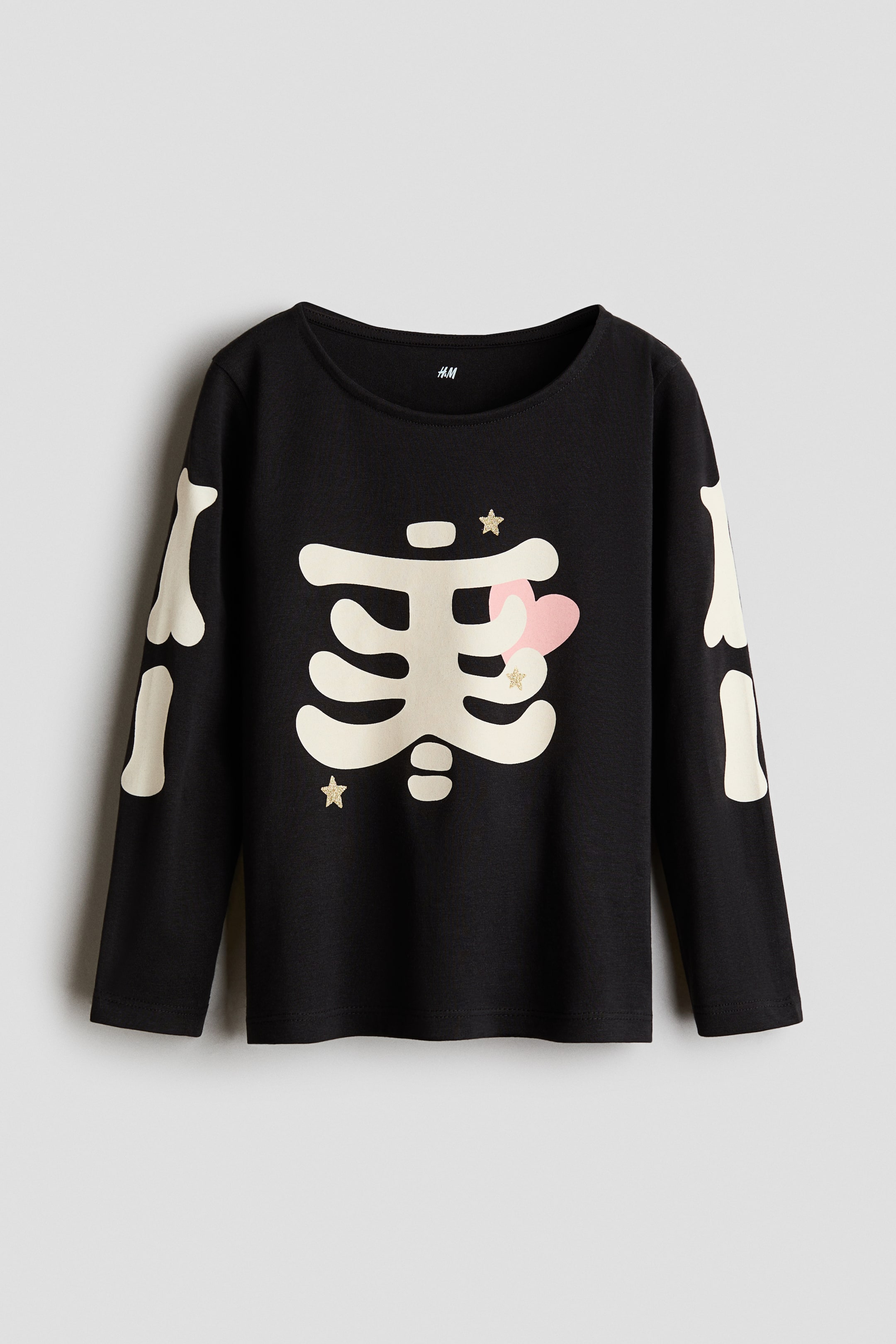View larger image: A black long-sleeved top features a cream-colored skeleton design on the front. The design includes a rib cage with a pink heart and gold glitter stars, and the arm bones extend along the sleeves.