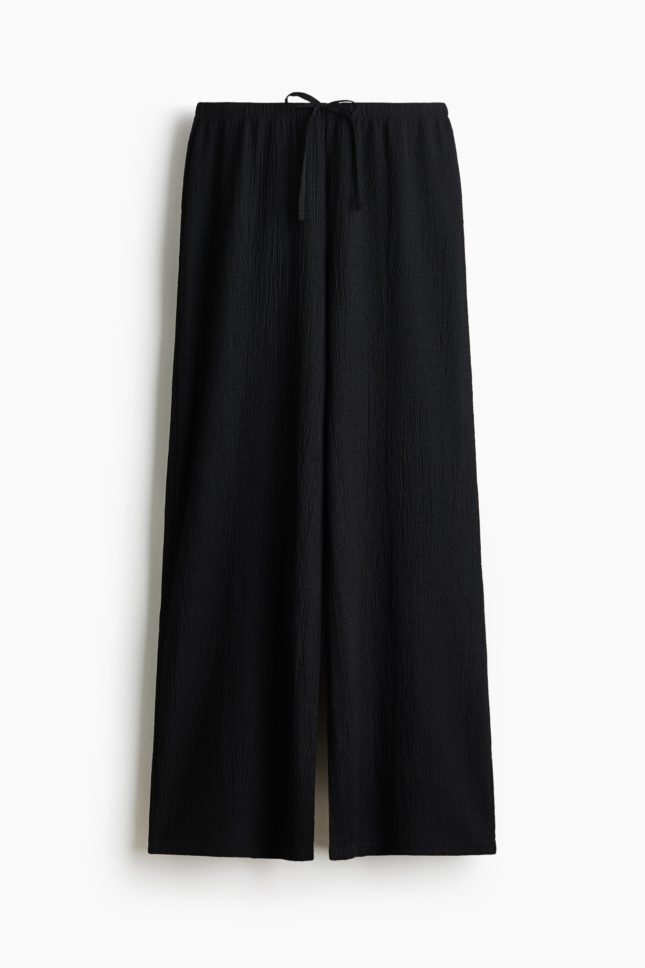 View larger image: Black wide-leg pants are displayed front-facing, showcasing an elastic waistband with a visible drawstring and a consistent crinkled texture throughout.