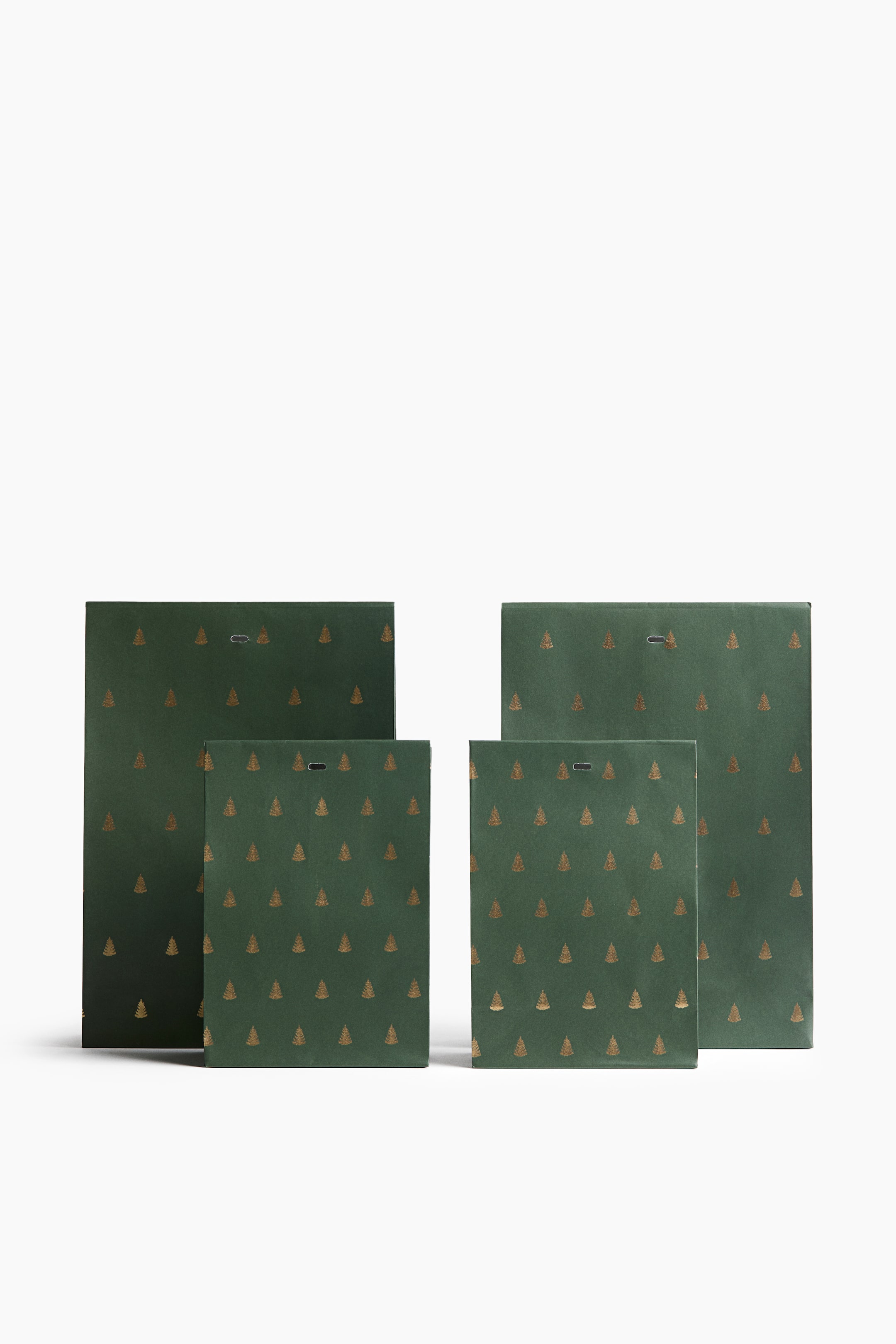 View larger image: A set of four dark green paper gift bags, featuring two large and two small bags, is standing upright in a front view. Each bag is decorated with a repeating pattern of small gold-foil Christmas trees and features a folded top with a pre-punched horizontal oval hole.