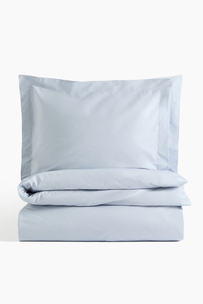 A light blue duvet cover set is presented, featuring a neatly folded duvet cover at the bottom and a single pillowcase resting on top. The pillowcase showcases a distinct border along its edges, and the fabric appears smooth and crisp. - 1