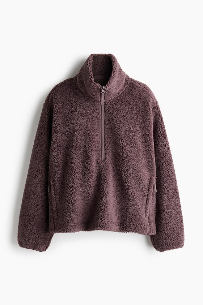 A mauve-colored fleece pullover is facing front, featuring a high stand-up collar and a tonal half-zip closure. The long-sleeved garment is displaying a textured sherpa finish, a relaxed boxy fit, and subtle zippered side pockets. - 1