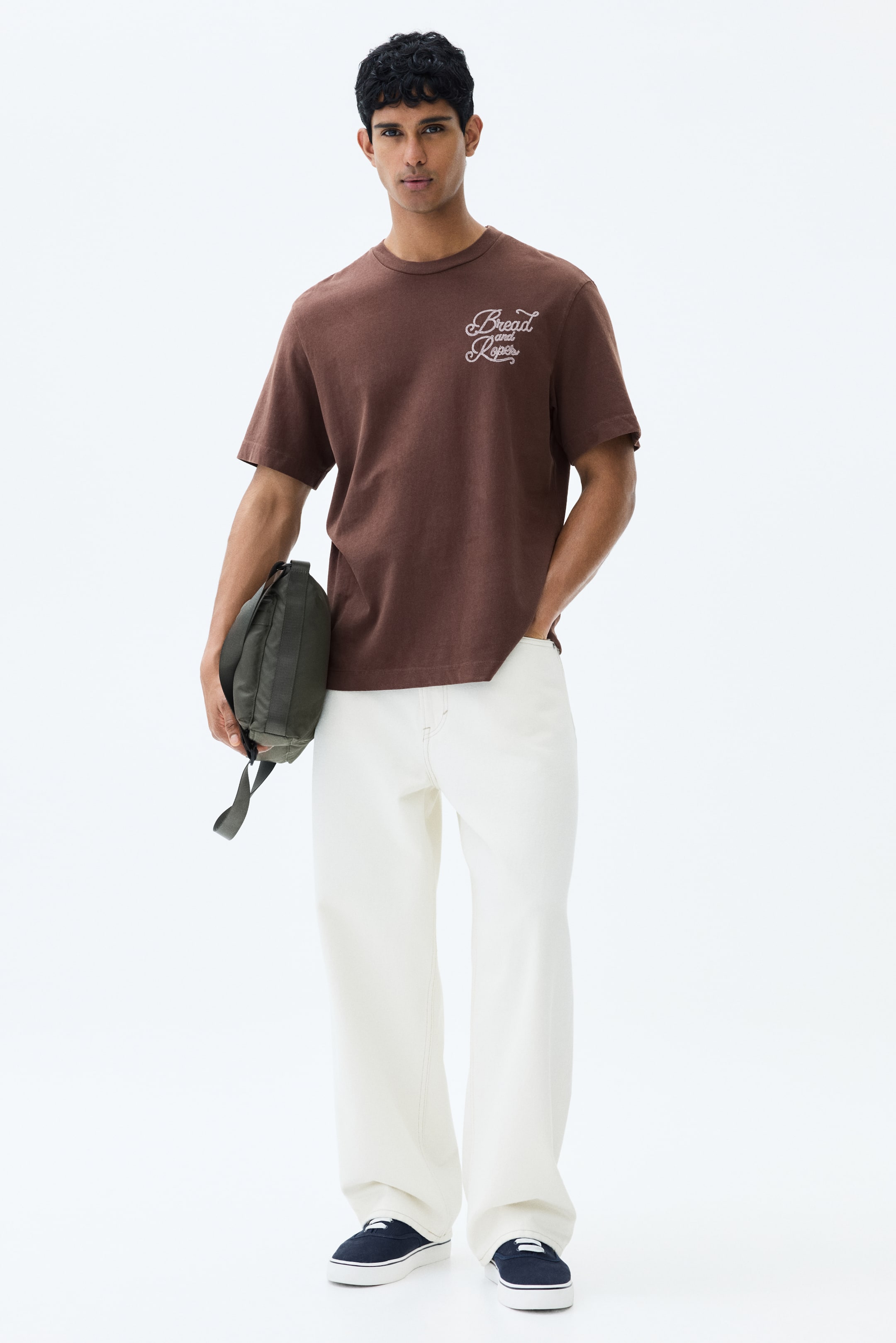 View larger image: The model is wearing a brown T-shirt featuring a round, rib-trimmed neckline, dropped shoulders, and a straight-cut hem. On the front, there's an embroidered motif with the words 'Bread and Ropes'. The T-shirt offers a regular fit.