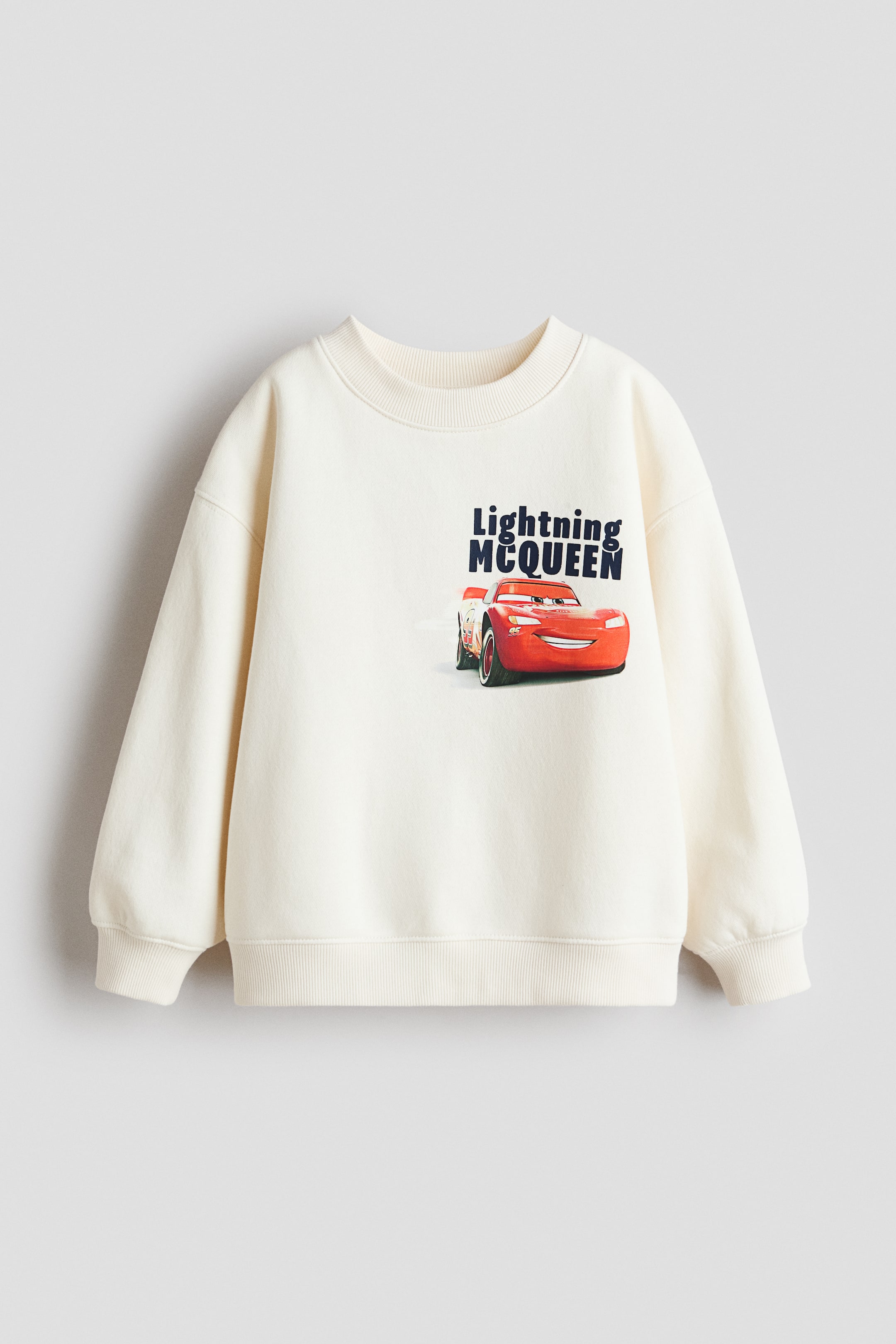 View larger image: The front of a cream sweatshirt displays a "Lightning McQueen" print, featuring the red car character and text. It is designed with a round, rib-trimmed neckline, dropped shoulders, long sleeves, and ribbed cuffs and hem.