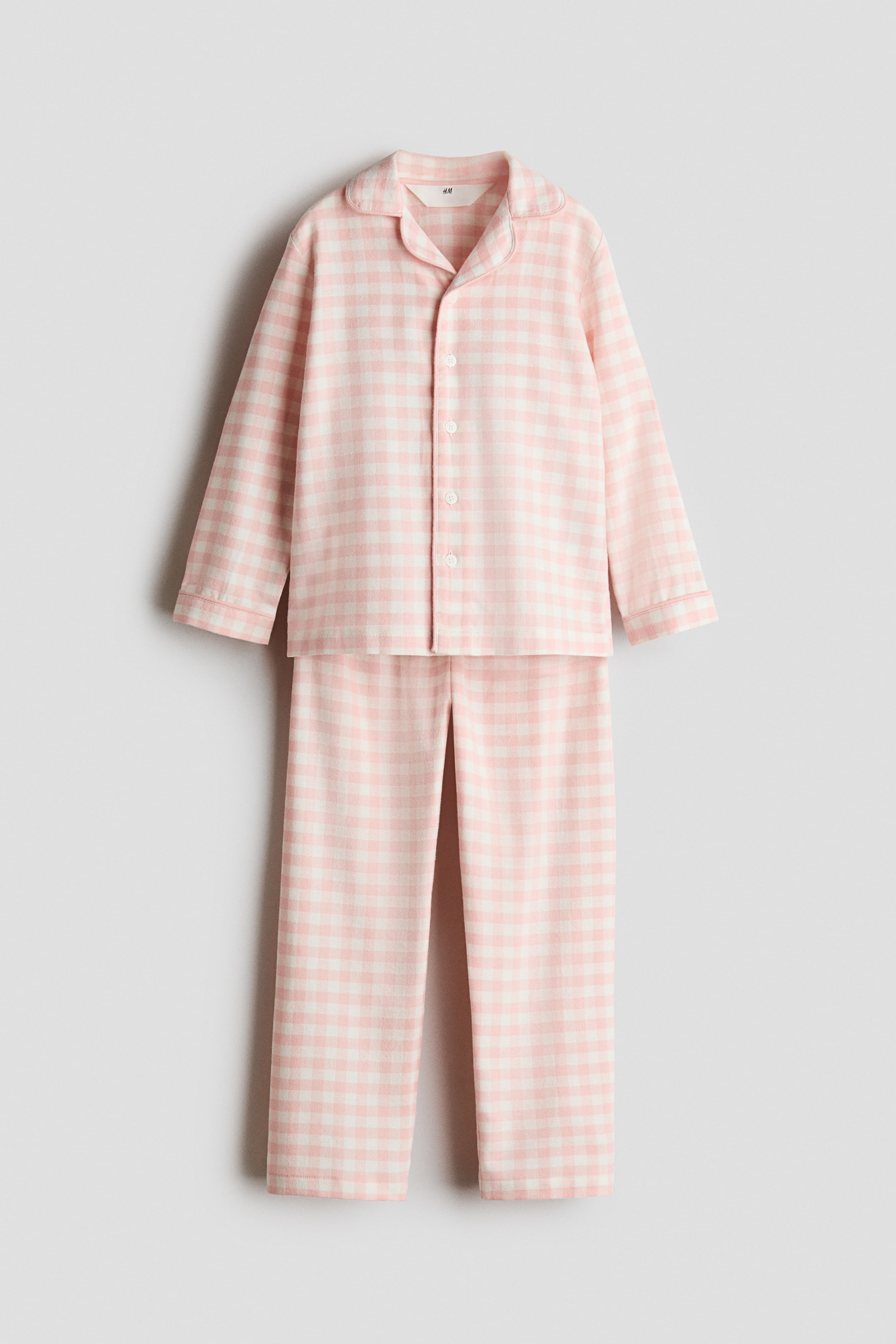 Agrandir l'image: Un ensemble de pyjama à carreaux vichy rose et blanc est posé à plat et orienté vers l'avant. Le haut à manches longues présente un col arrondi et une fermeture boutonnée sur le devant, et le pantalon long assorti affiche une coupe droite.