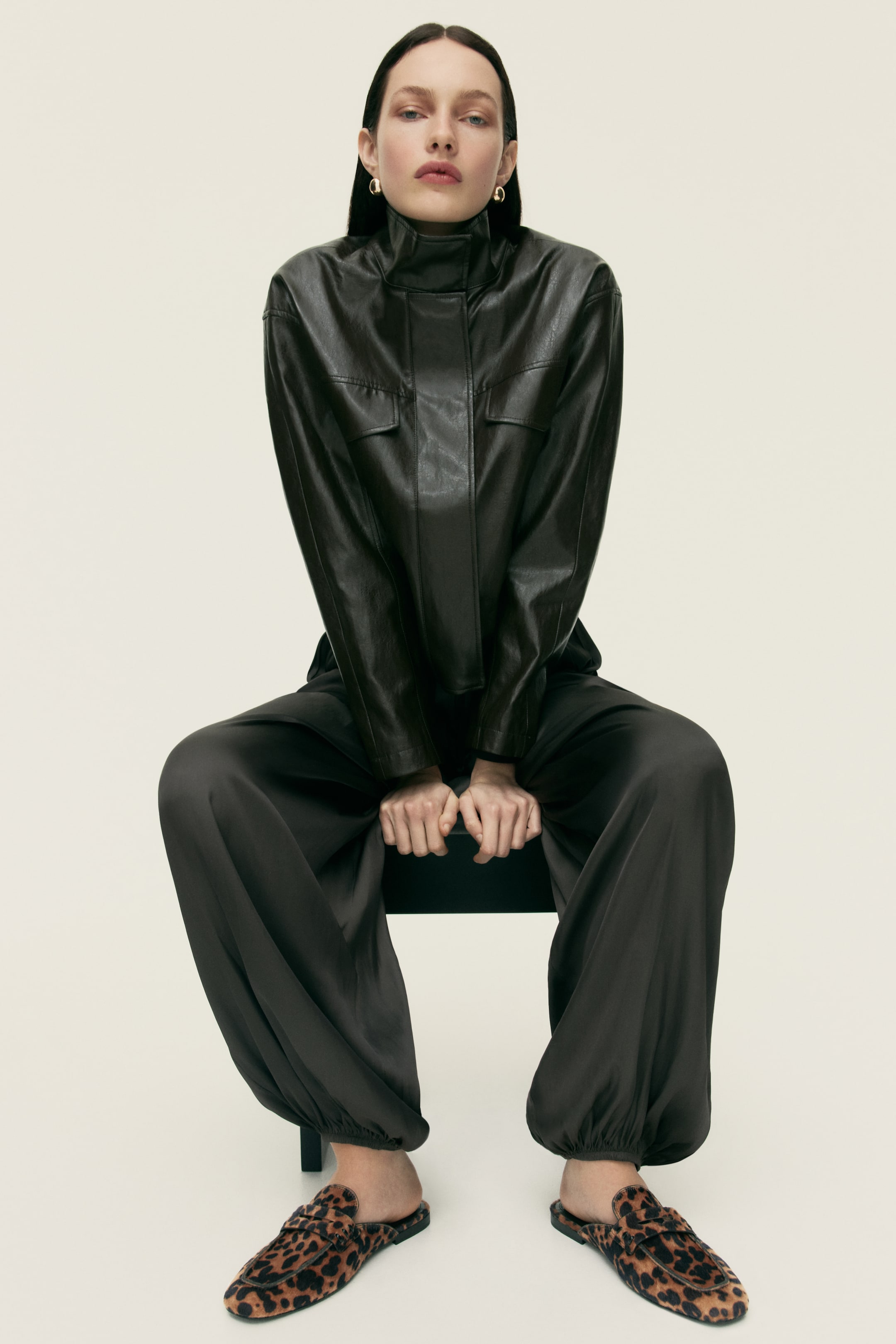 View larger image: A dark brown leather-look high-neck top features two flap chest pockets. It's styled with dark brown wide-leg trousers that showcase gathered elasticated ankles, and leopard print mule loafers with a gold-toned bar across the vamp.