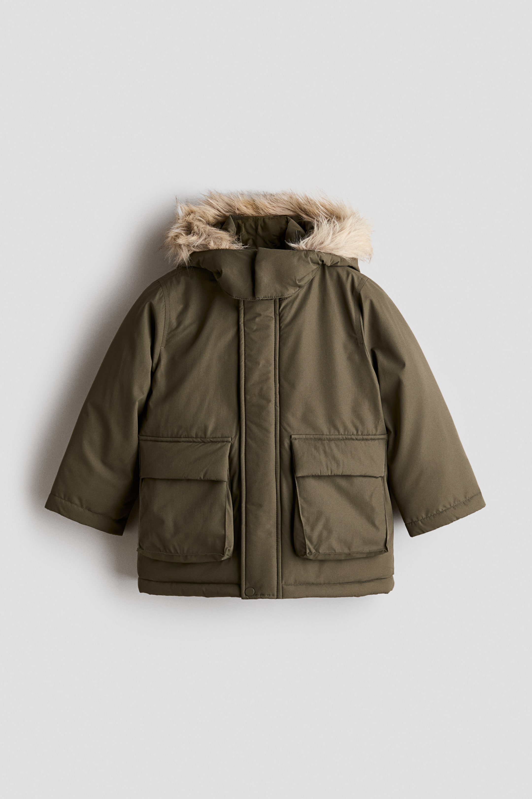 Ver imagen más grande: Una parka verde oliva está colocada de frente, con capucha con ribete de pelo sintético marrón claro y cierre oculto en el centro delantero. La chaqueta acolchada muestra dos grandes bolsillos de parche delanteros con solapas y mangas largas y lisas.