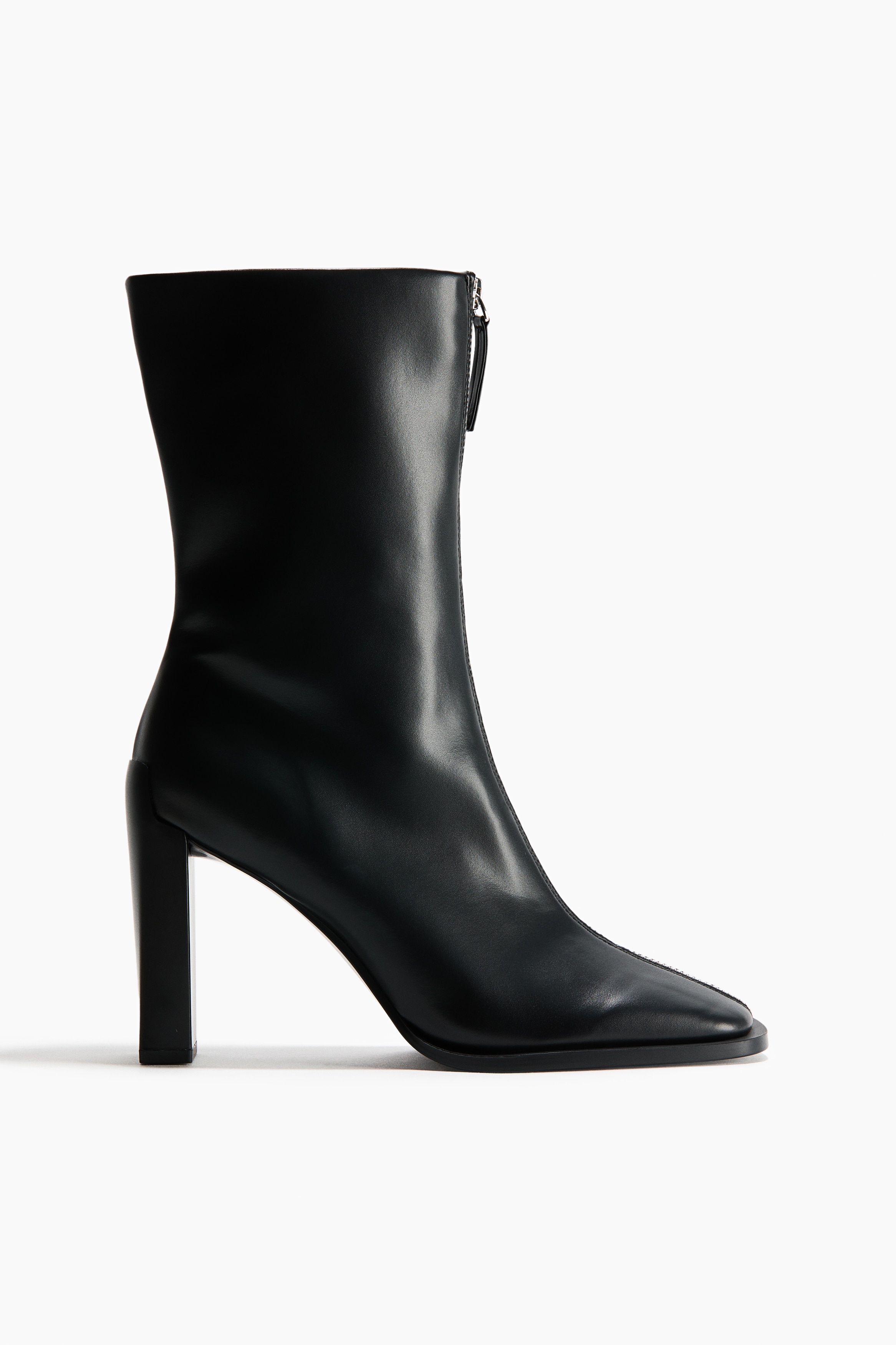 Black block-heeled ankle boots in a smooth coated fabric are being worn by the model. The boots feature a square-toe design, chunky block heels, and a prominent silver-tone zip running down the centre front.