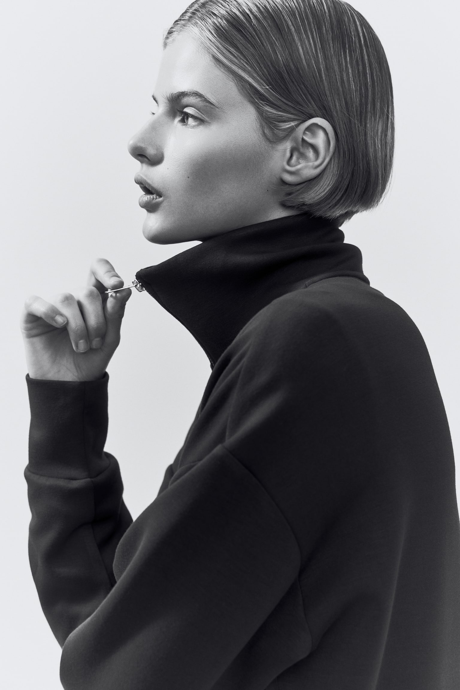 A loose-fit, dark brown track jacket is shown front-facing, featuring a stand collar and a silver zip extending down the front. It displays dropped shoulders, long sleeves with double-layered cuffs, and a double-layered hem. - 1