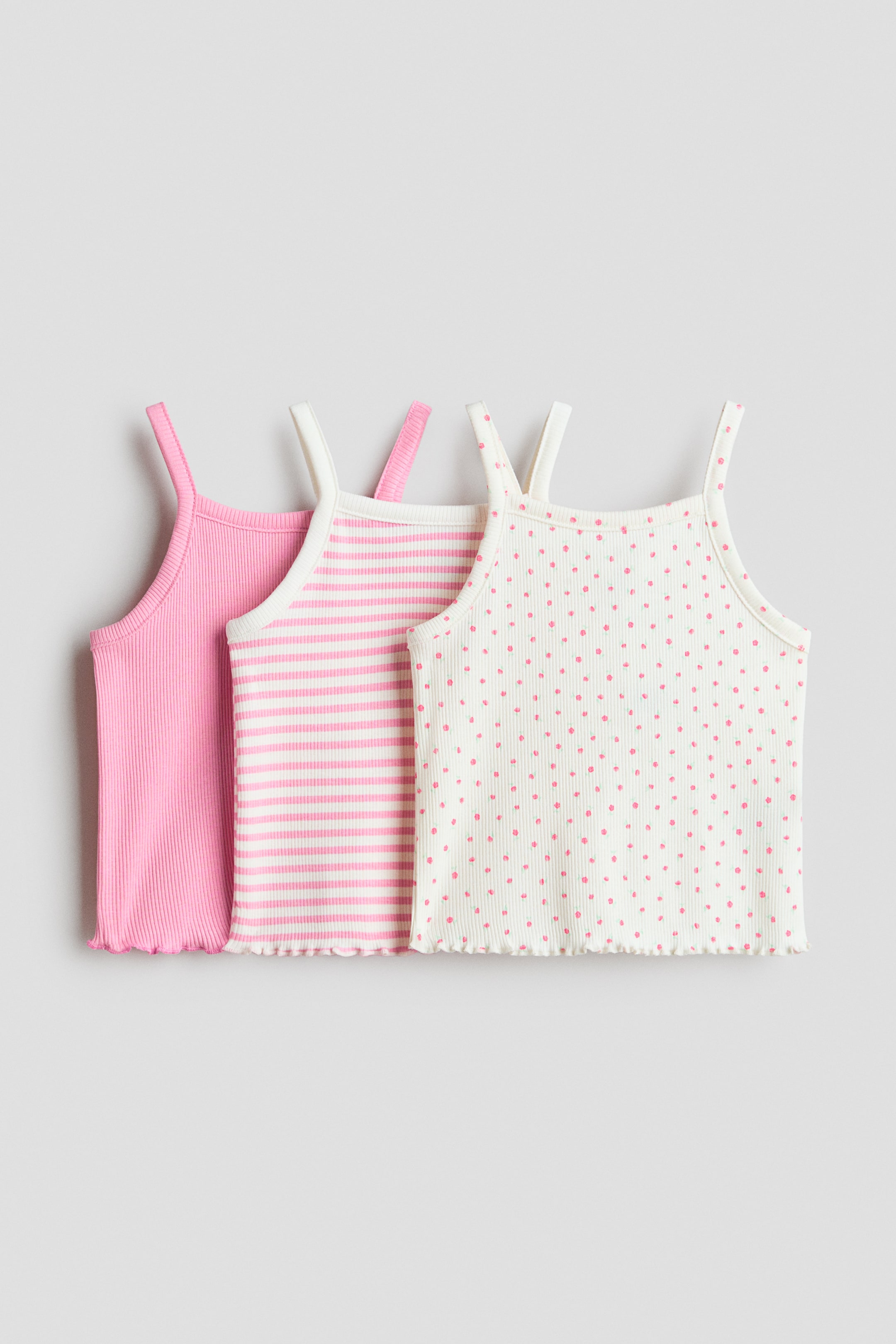 View larger image: Three ribbed tank tops are showcasing their front sides, each adorned with slender shoulder straps and a frilled hem. The first is a solid pink, the second is off-white with pink horizontal stripes, and the third is off-white with pink polka dots.