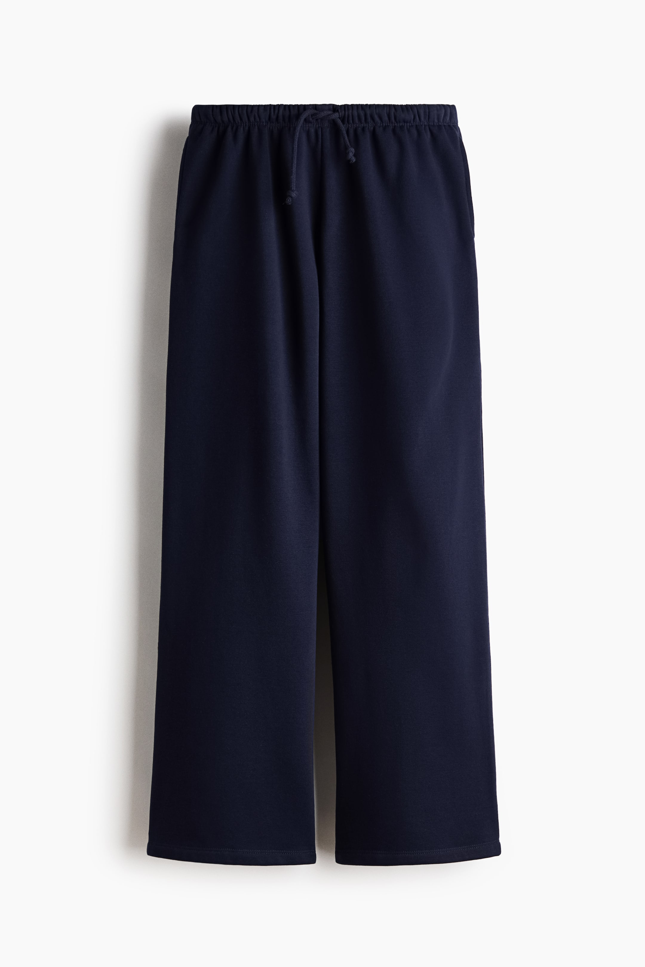 View larger image: Navy blue, loose-fit joggers are displayed from the FRONT, showcasing an elasticated drawstring waist with a visible tie, discreet side seam pockets, and wide, straight legs in a sweatshirt fabric.