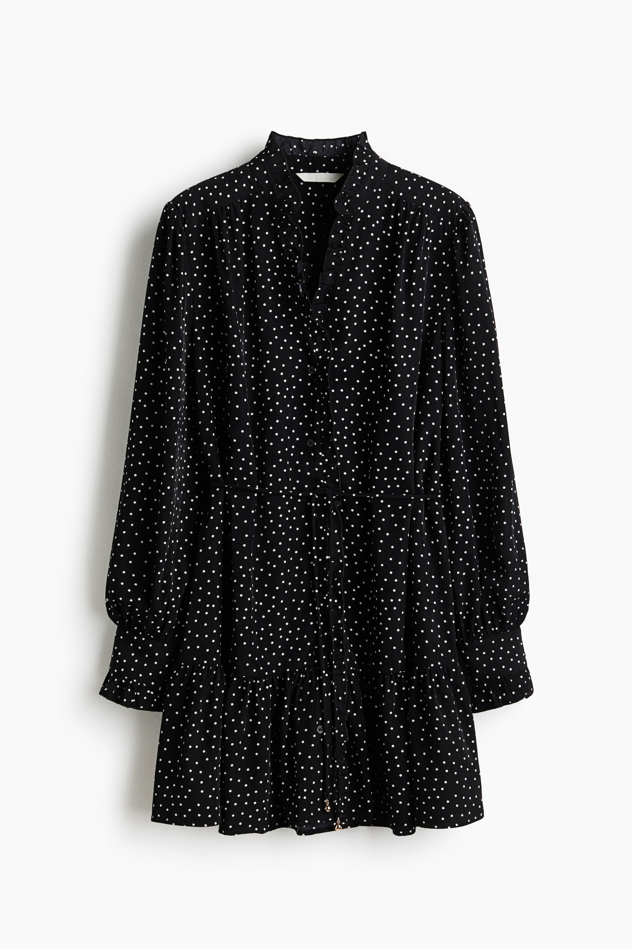 View larger image: The black dress, covered in white polka dots, is presented from the front, featuring a ruffled band collar and a button-front V-neck placket. It is designed with long voluminous sleeves gathered into elasticated ruffled cuffs, and a tiered skirt with a ruffled hem.