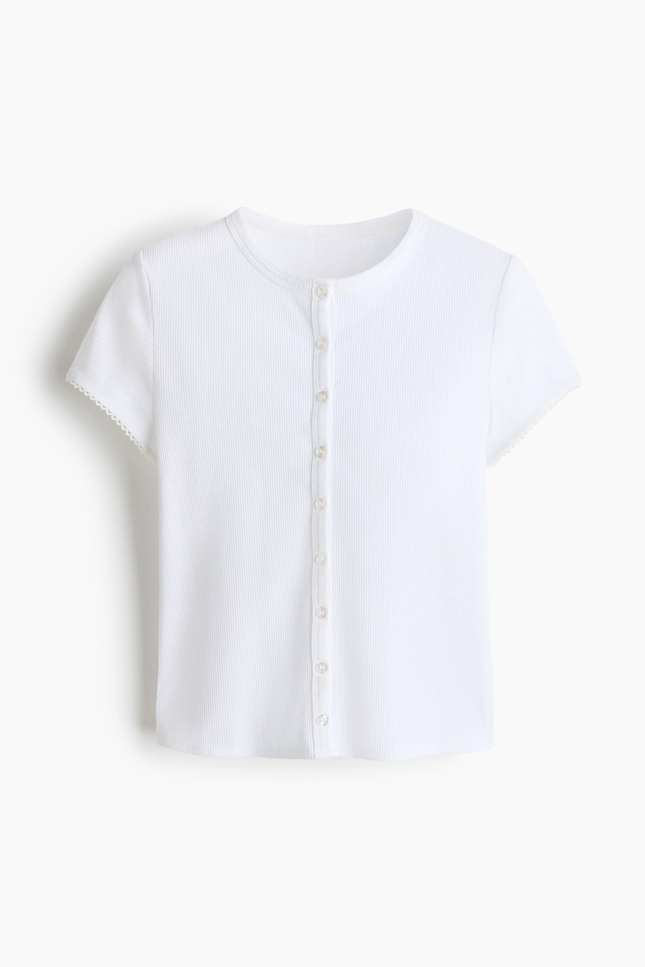 Xem ảnh lớn hơn: Một chiếc áo trắng, ngắn, ôm sát, làm từ vải cotton jersey gân được hiển thị từ phía trước. Nó có đặc điểm là cổ tròn, hàng nút ở phía trước, tay ngắn với viền xếp nếp tinh tế, và gấu áo cắt thẳng.