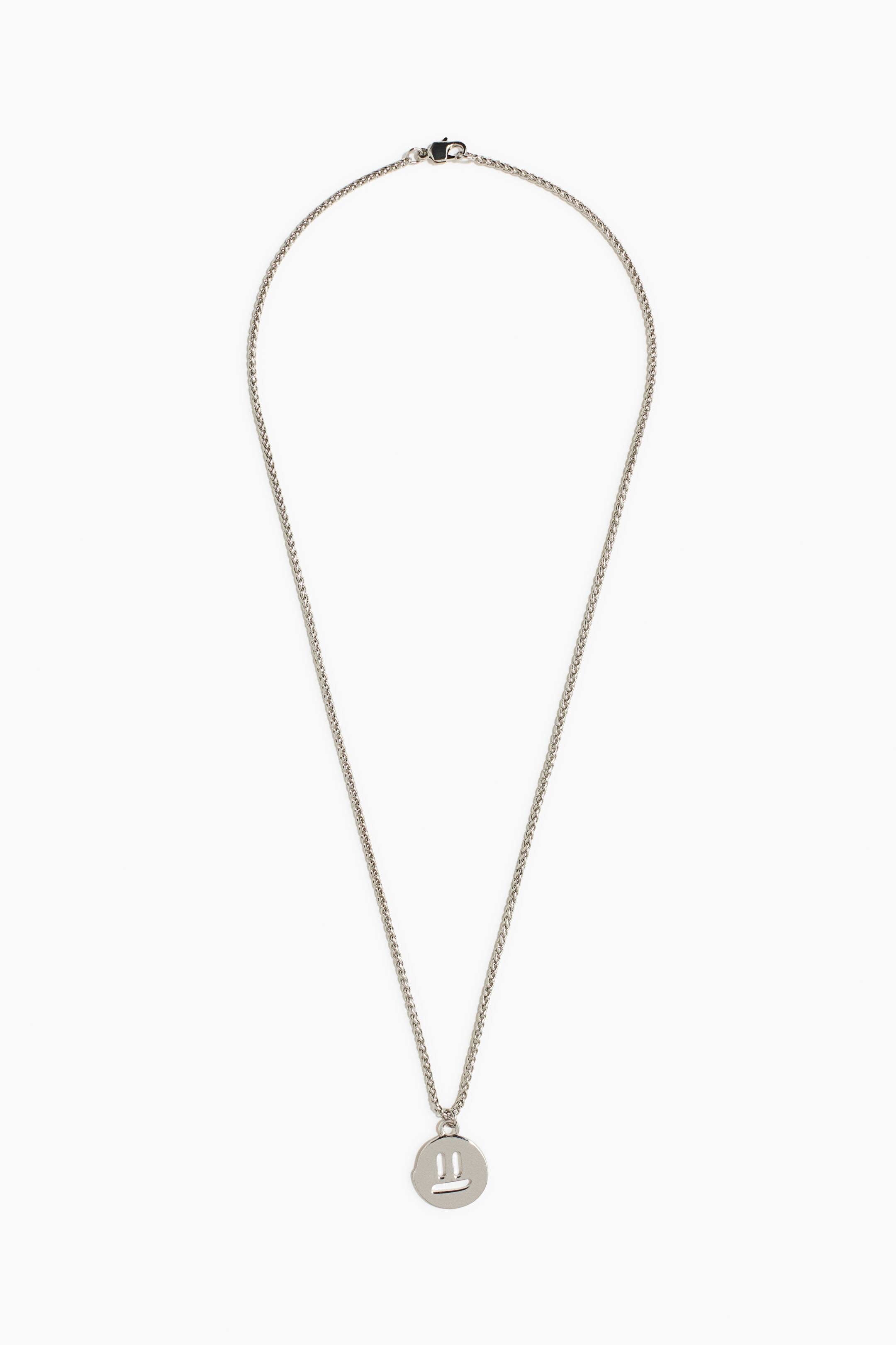 View larger image: A silver-toned necklace features a fine wheat chain with a small lobster clasp. A round, flat pendant hangs from the chain, displaying a simplified face design with two vertical lines for eyes and a horizontal line for a mouth.