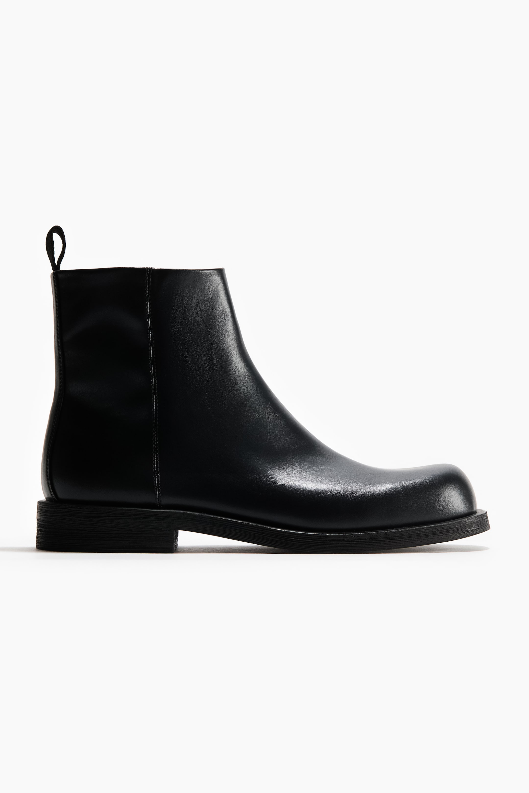 View larger image: A black ankle boot is facing right, angled slightly from the side, showcasing its smooth black leather, rounded toe, low stacked heel, and a black pull tab at the back of the shaft.
