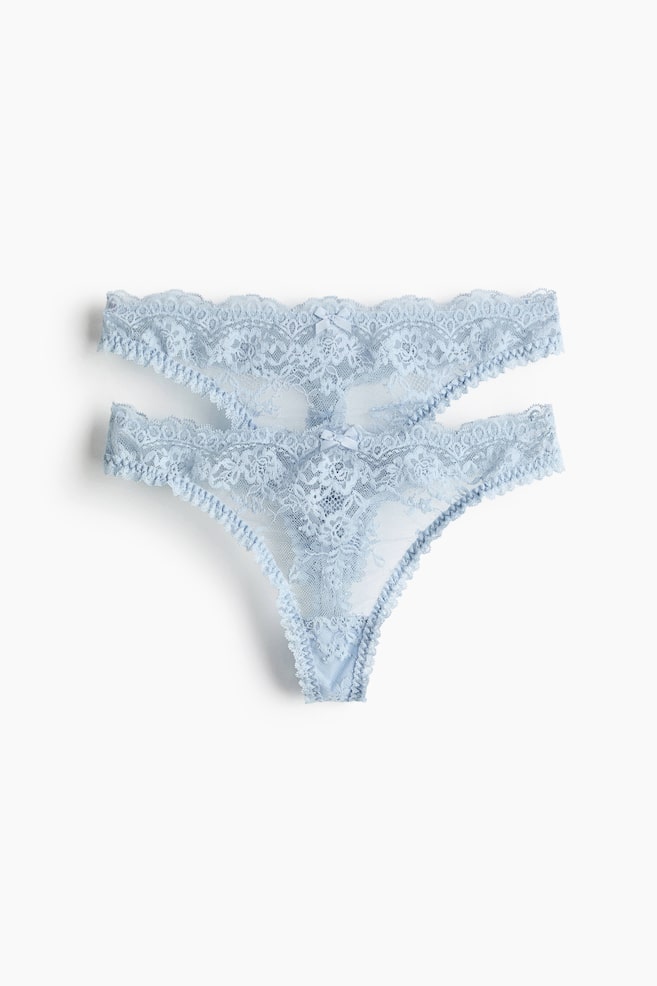 Two light blue thong briefs showcase sheer lace with intricate floral patterns, presented front-facing. Each brief is designed with a low waist, a lined gusset, and a small bow at the front centre of the waistband. - 1