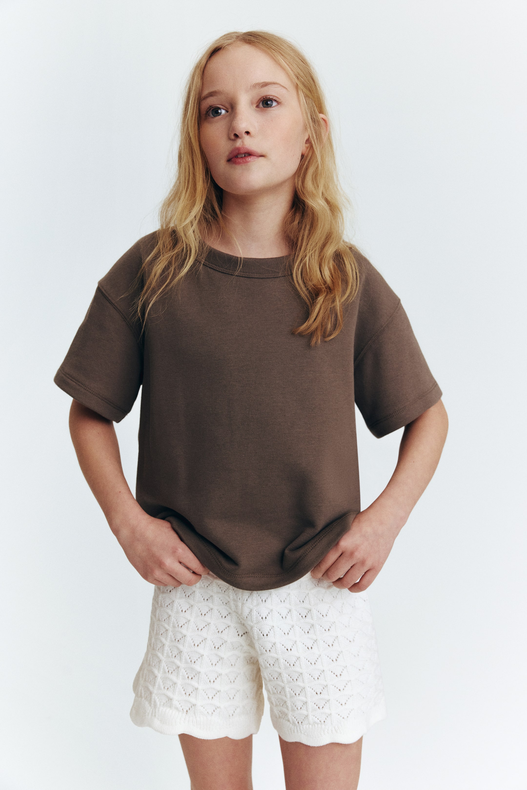 View larger image: A dark brown short-sleeve t-shirt is presented from the front, featuring a ribbed crew neck. The oversized t-shirt's hem is slightly lifted by hands, highlighting its relaxed fit.