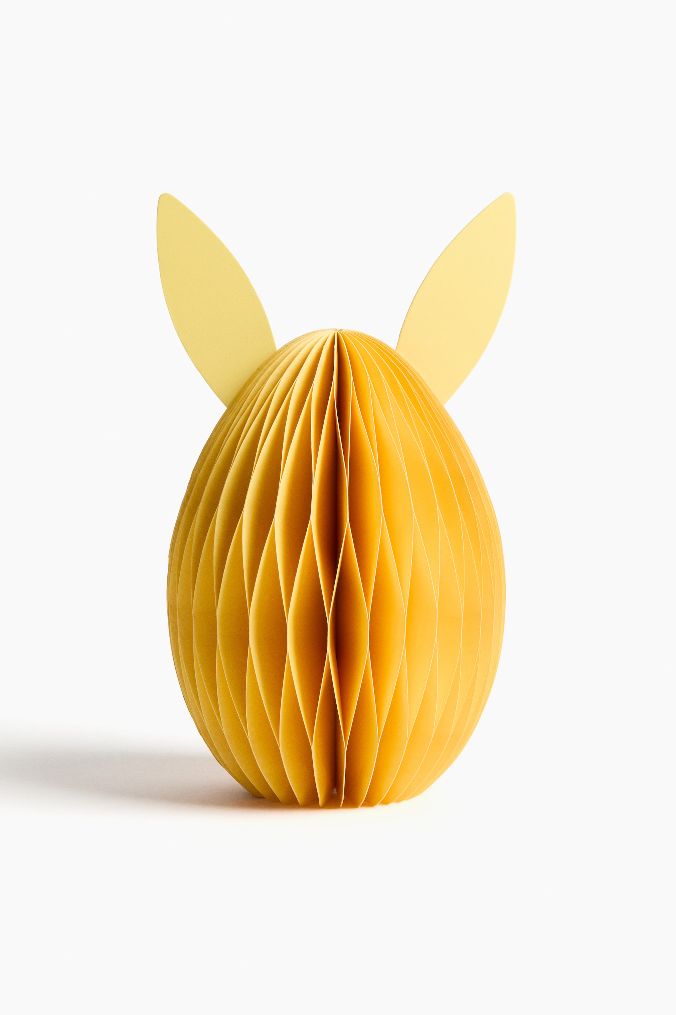 View larger image: A yellow honeycomb paper decoration features an ovoid body constructed from folded paper sections, with two flat, pointed, ear-shaped cutouts extending from its top, all presented front-on.