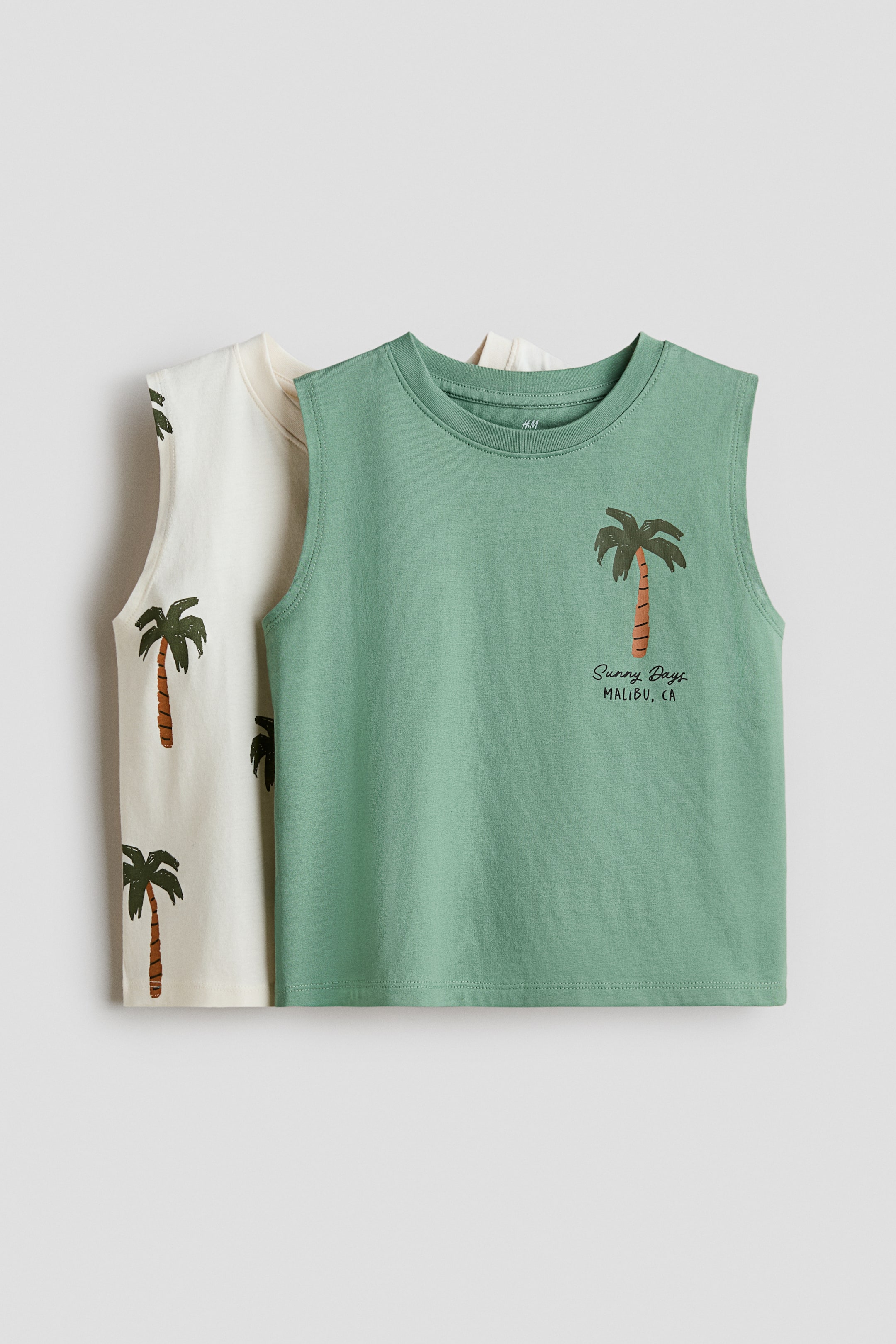 View larger image: Two sleeveless crew neck tops are showcased, layered with one in front of the other. The top in front is a sage green, adorned with a palm tree graphic and the text "Sunny Days MALIBU, CA" on its upper left front. The off-white sleeveless top behind it features multiple scattered palm tree graphics across its front surface.
