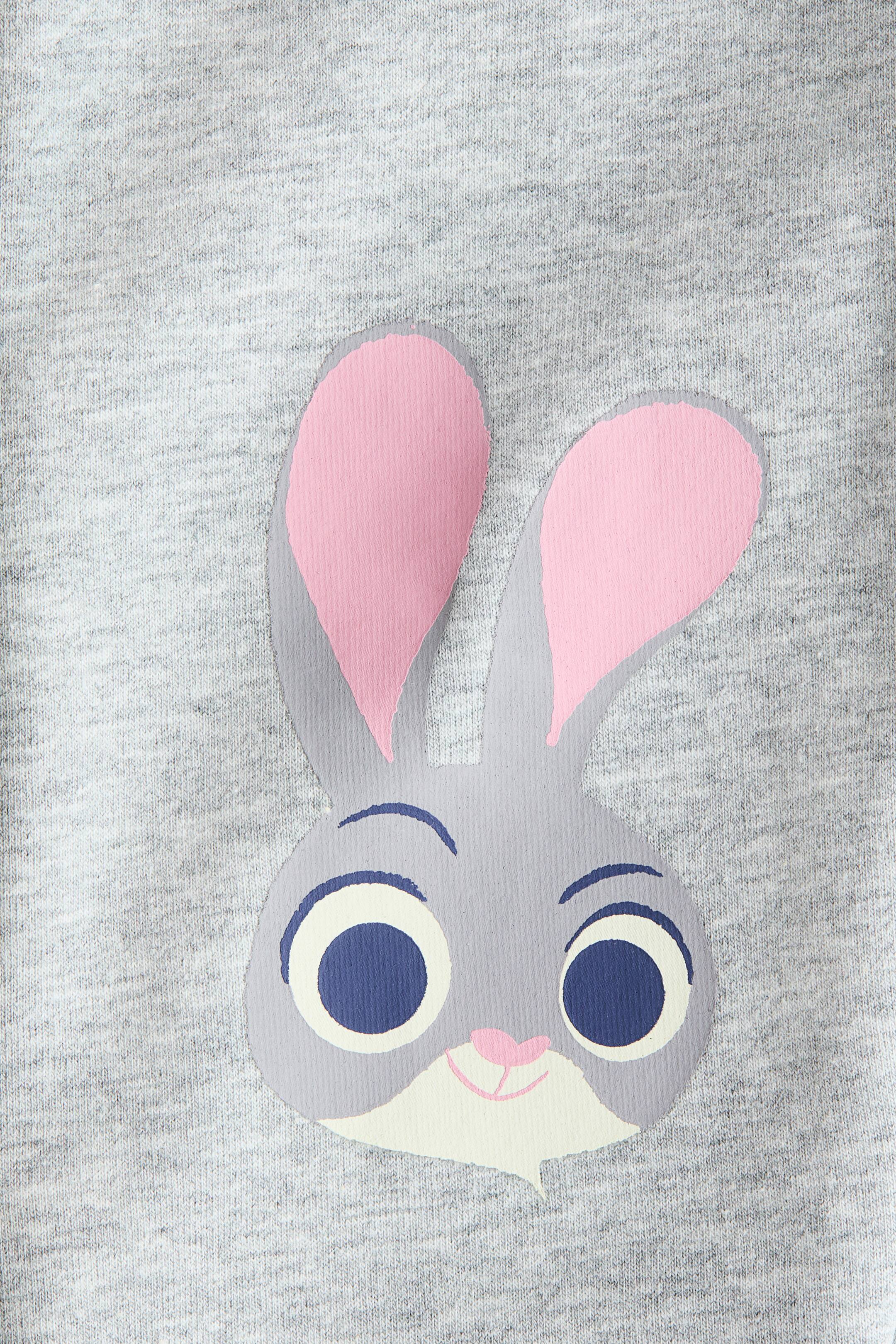 拡大画像を表示: ヘザーグレーの生地には、正面を向いた漫画のウサギの頭のプリントが表示されています。ウサギの顔は淡い灰色で、大きなピンクの内耳、濃い青色のアーチ形の眉毛、白い強膜と濃い青色の虹彩、小さなピンクの鼻と口、そして淡いクリーム色のあごの部分が特徴です。
