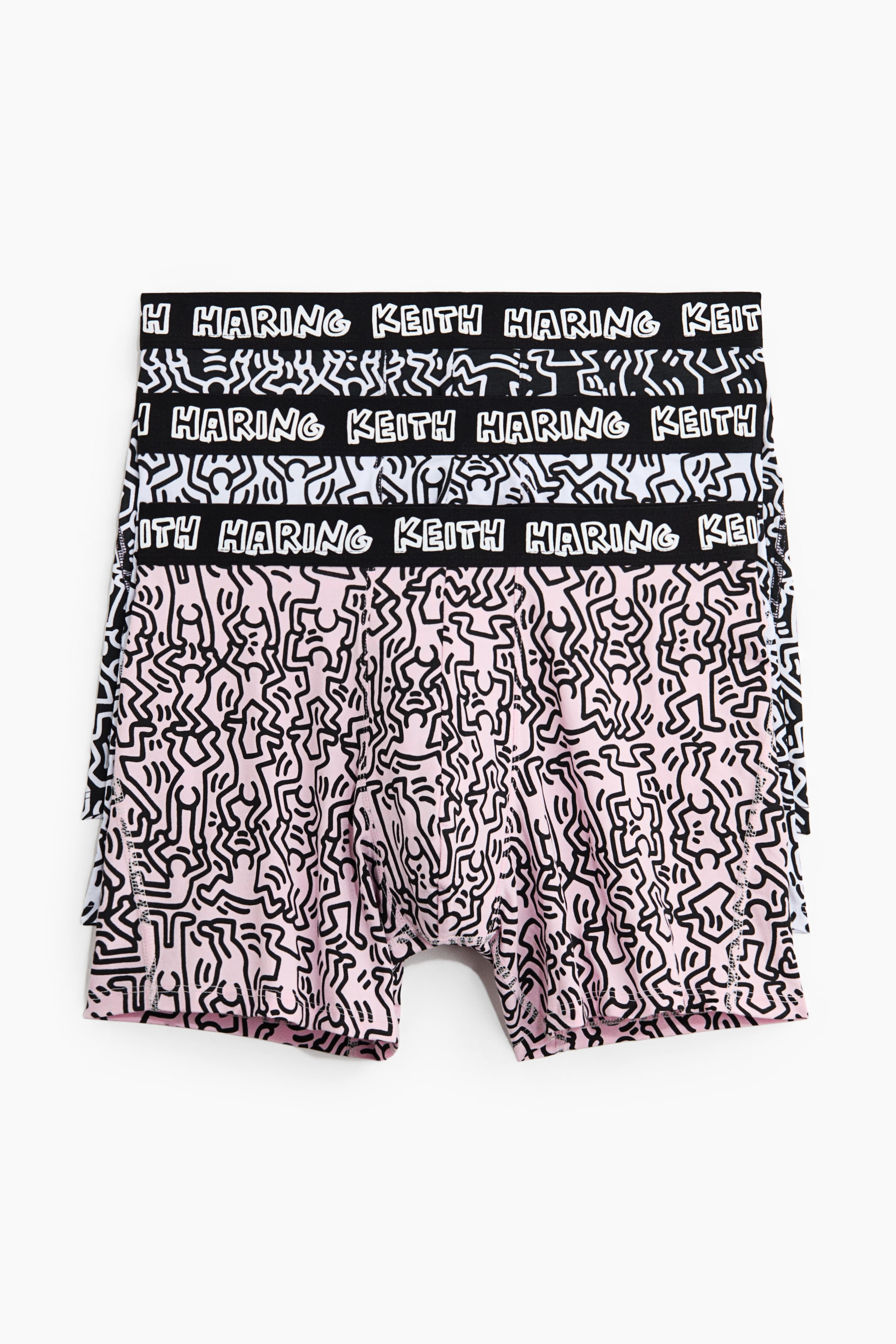 View larger image: A stack of boxer briefs is showcasing its FRONT view, with the topmost pair being light pink and featuring an all-over black Keith Haring stick figure pattern. Its black elastic waistband is displaying "KEITH HARING" in white text, and two other pairs are visible underneath, presenting the same pattern on white and black fabric bases.