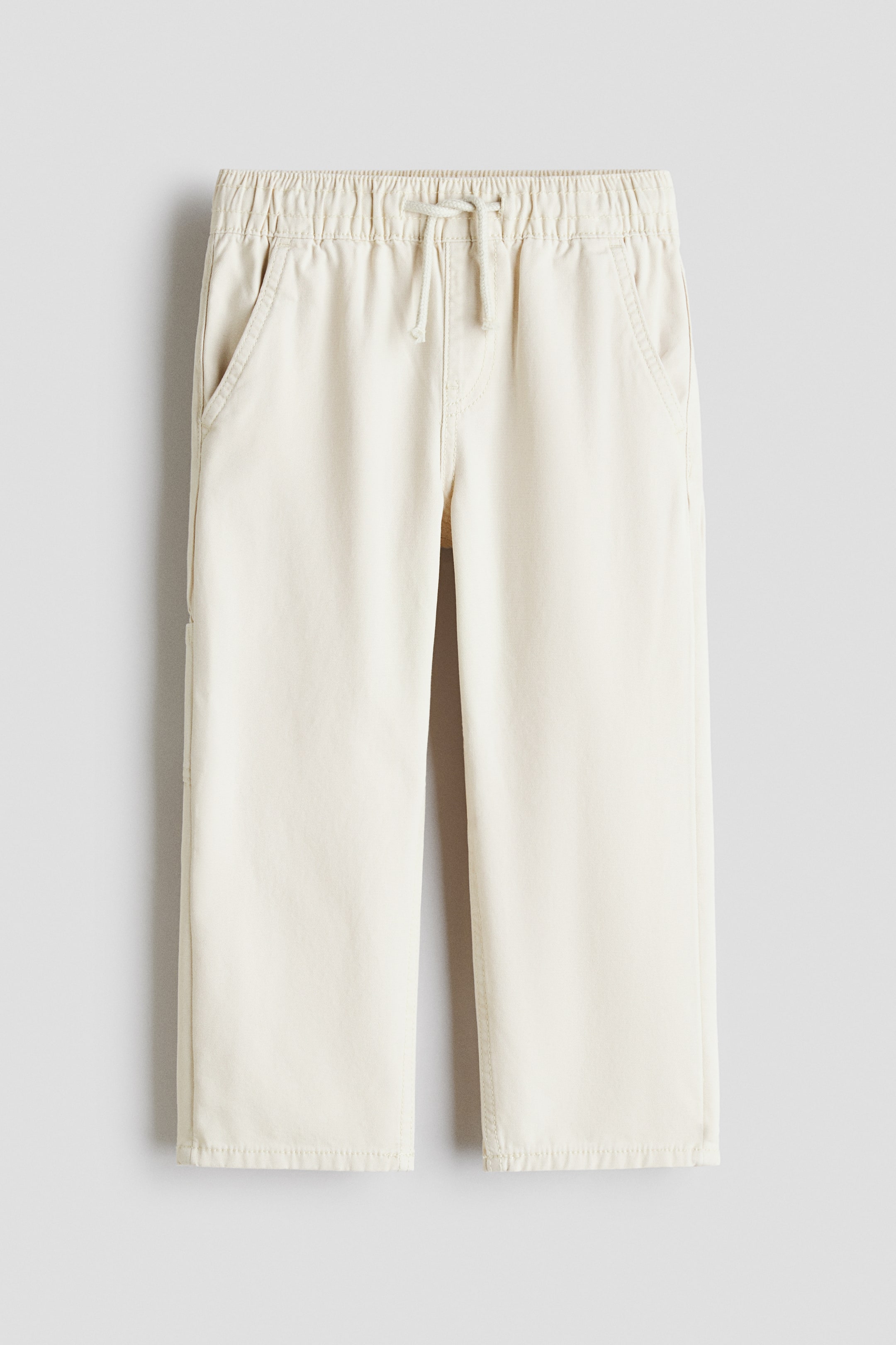 View larger image: Light cream trousers feature an elasticated waistband with a drawstring tie at the front, showcasing two angled front pockets and a straight leg cut with plain stitched hems.