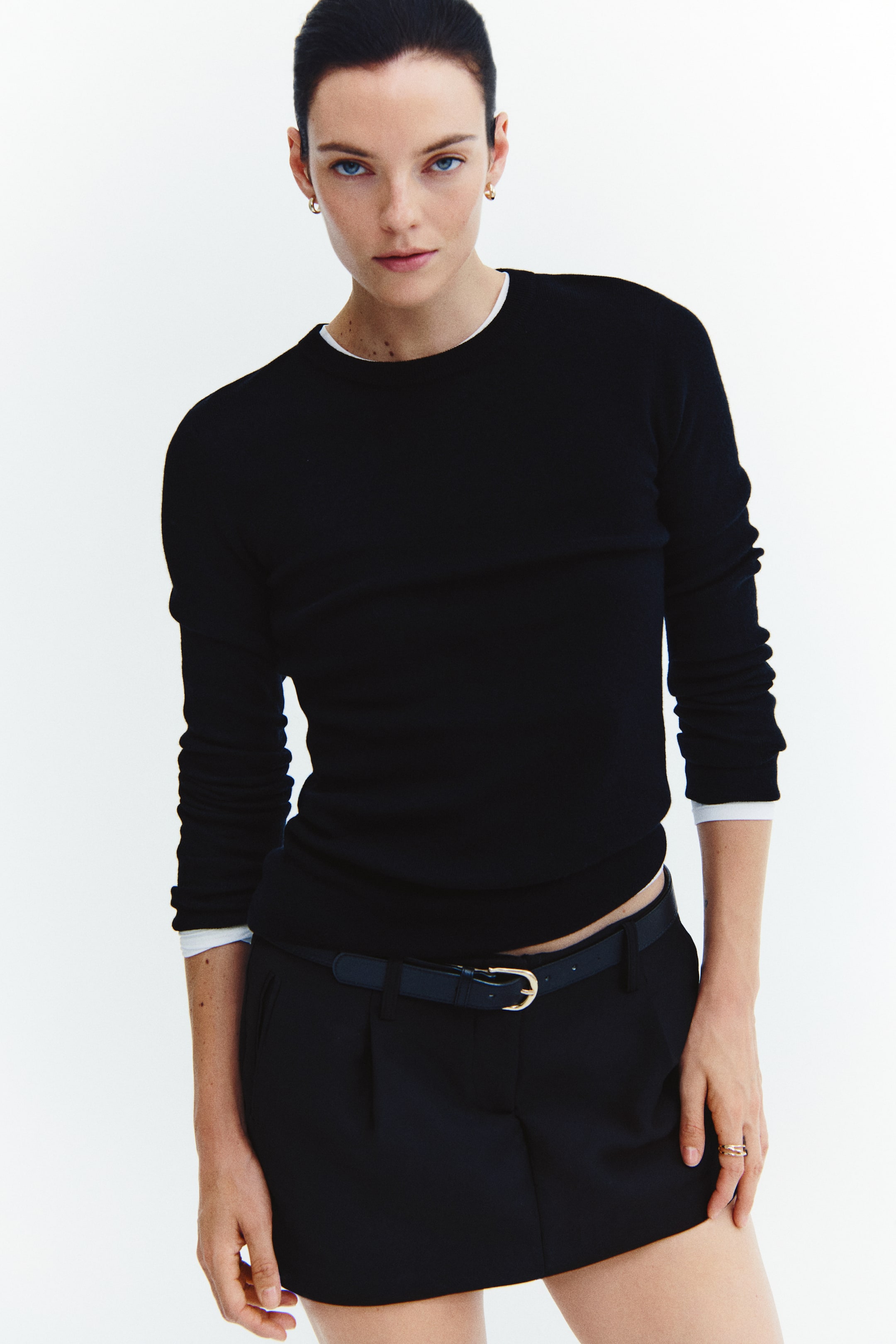 View larger image: A black fine-knit top made from a wool and cashmere blend is worn by the model, showcasing a round rib-trimmed neckline and long sleeves. The fitted top is layered over a white shirt visible at the neckline and cuffs, and paired with a belted black skirt.