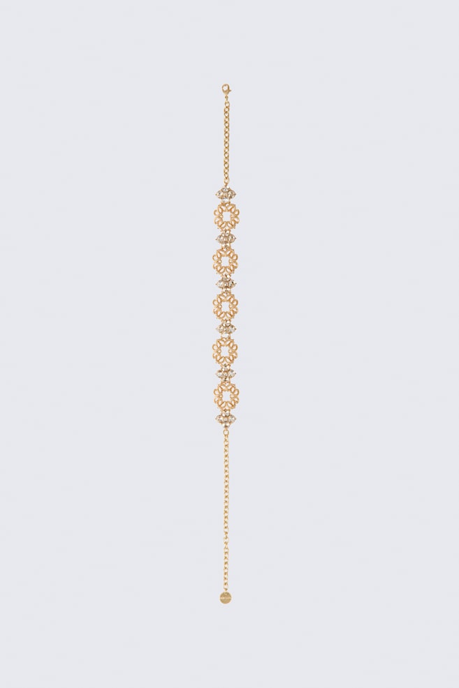 A short rhinestone necklace is laid vertically, showcasing alternating gold-tone openwork circular filigree links and rhinestone-embellished floral clusters. The necklace features a lobster clasp on one end of the chain and an adjustable extender chain with a small circular tag on the other. - 1