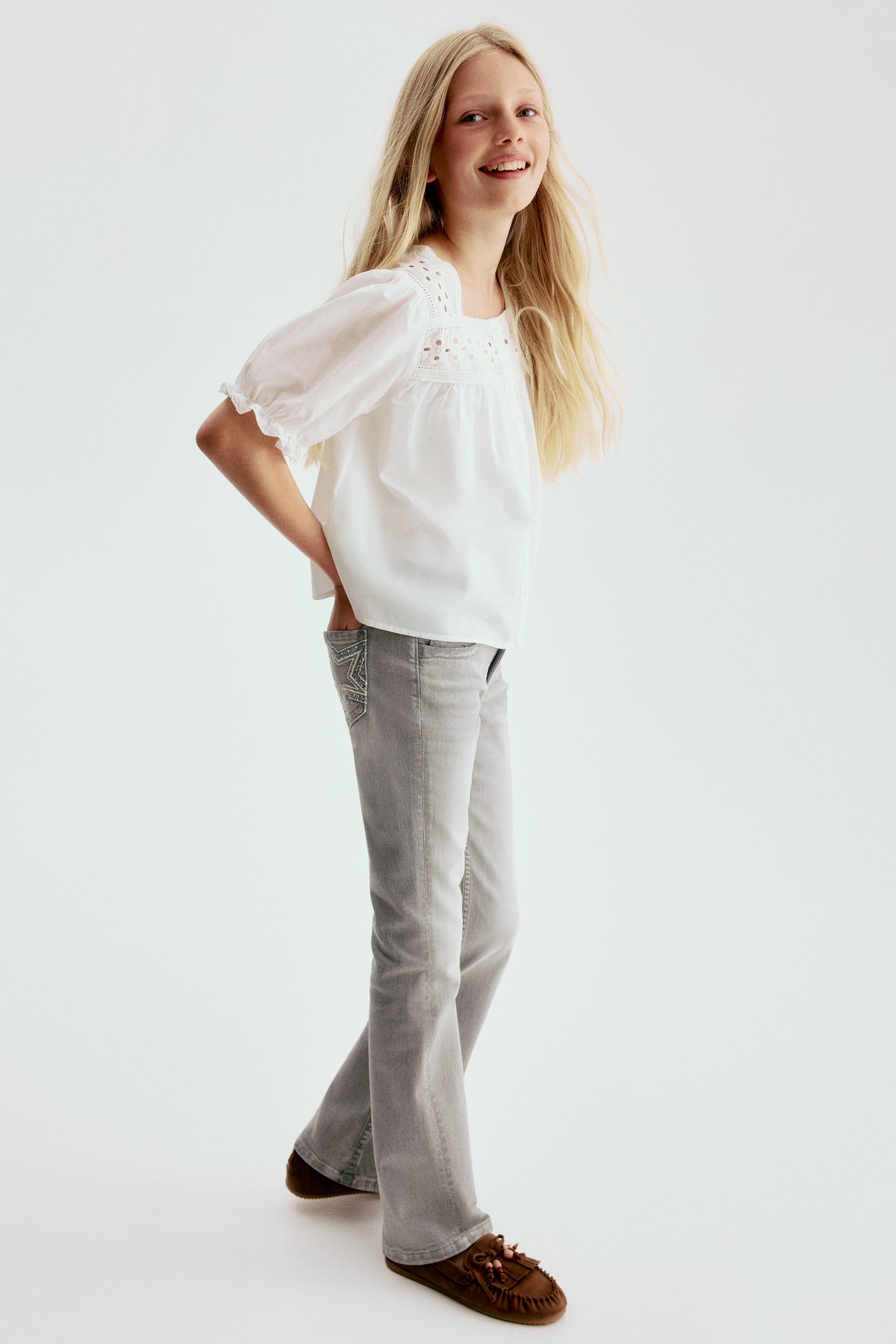 Voir une image plus grande: Jeans bootcut gris arborant un délavé gris clair avec une coupe ajustée au niveau de la cuisse, s'évasant sous le genou. Une poche arrière présente un motif d'étoile brodé avec des ornements scintillants.