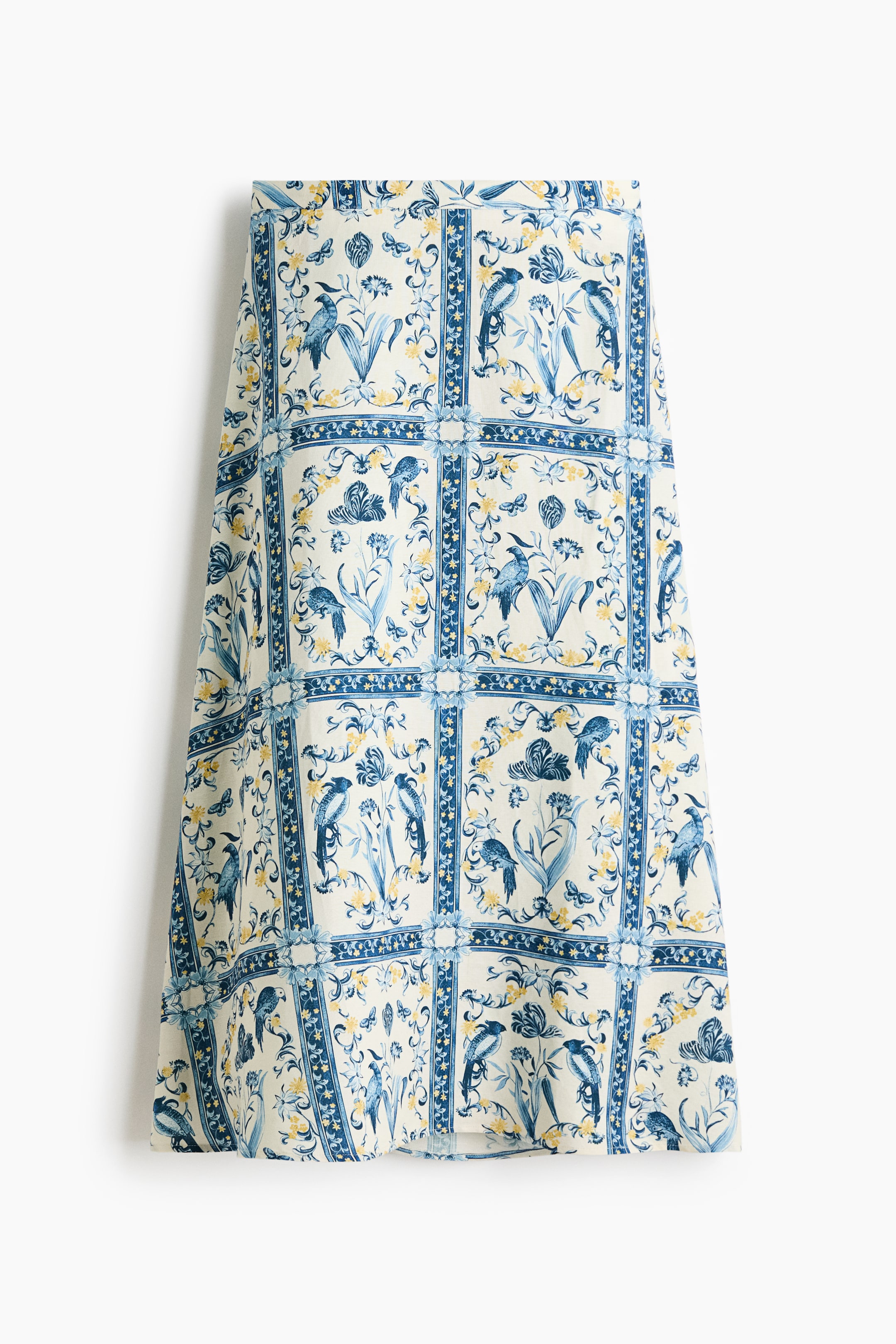 View larger image: The skirt is showcasing its front, featuring an elaborate blue and yellow botanical and bird print on an off-white background. The design is arranged in a grid of square panels containing birds, flowers, and butterflies, bordered by vertical and horizontal decorative stripes.