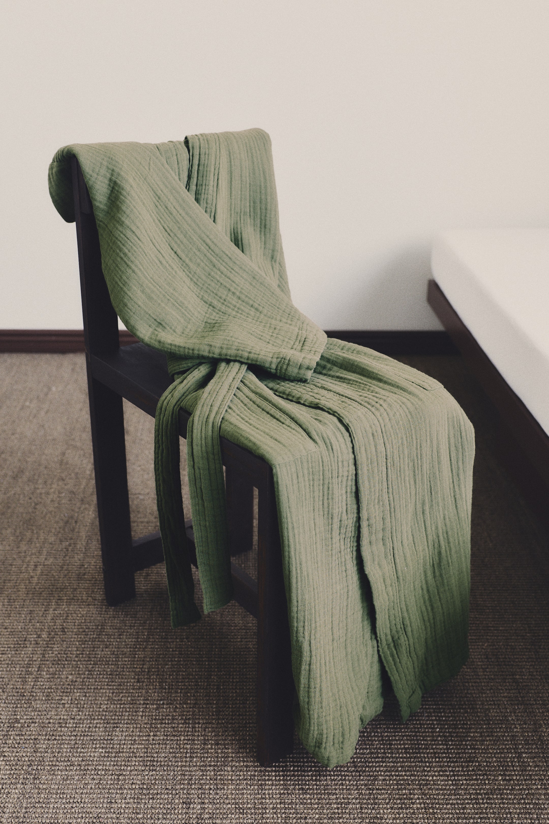 View larger image: A green cotton muslin dressing gown gracefully drapes, highlighting its soft, crinkled texture. A matching tie belt is neatly knotted around the folded garment.